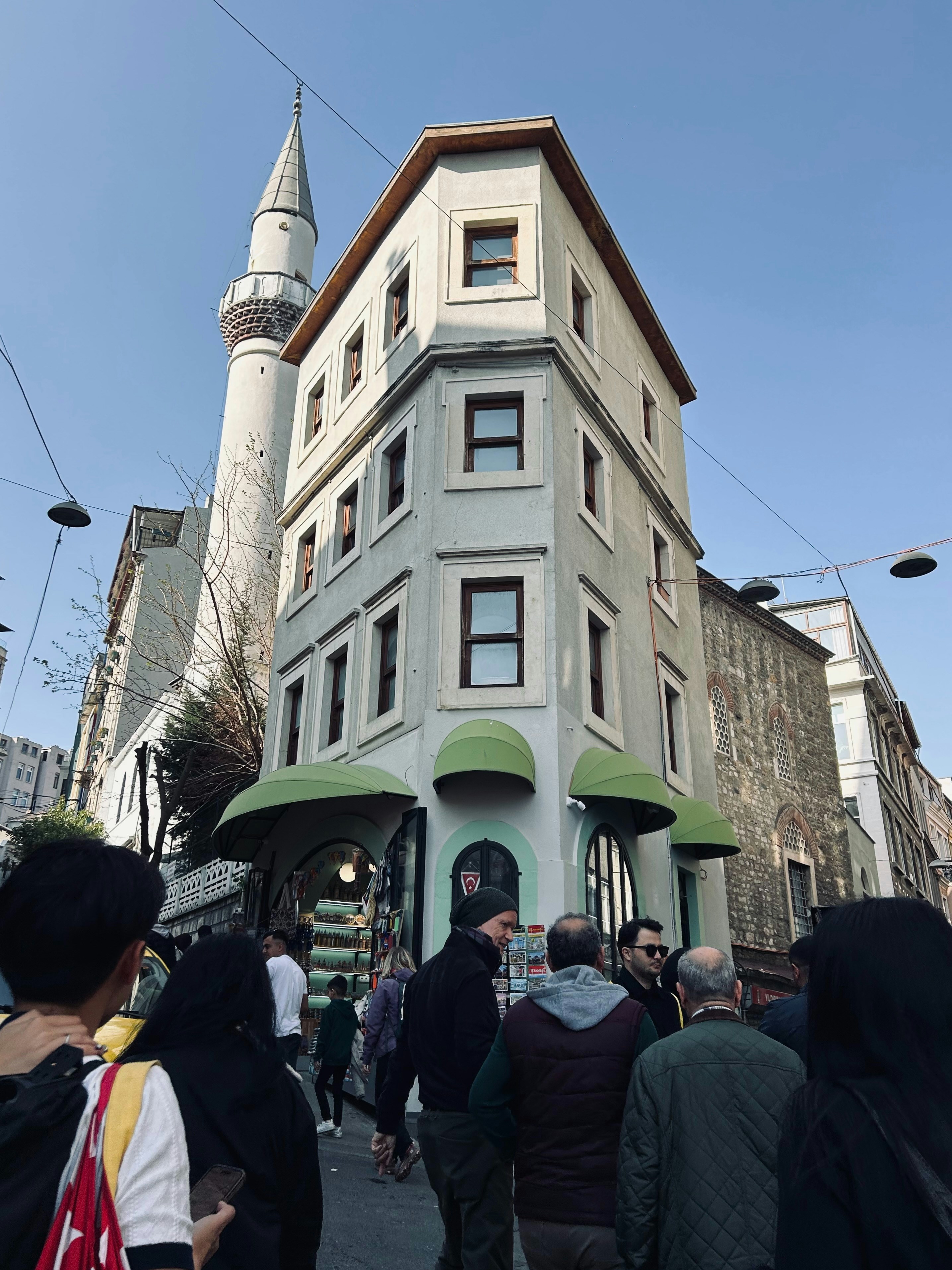 People walk near a corner building and minaret.
