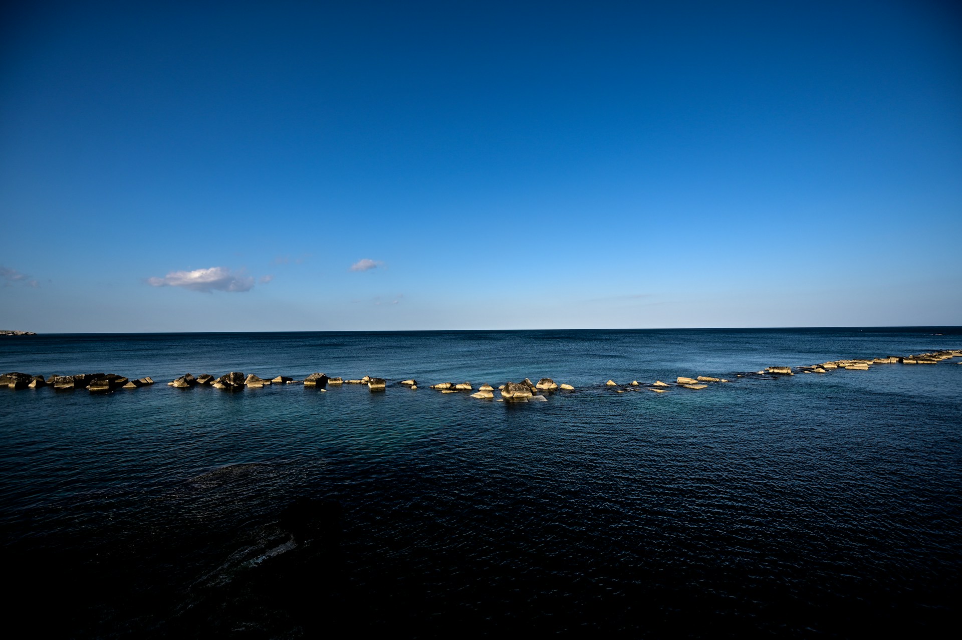 Blue ocean and sky, with a row of rocks.