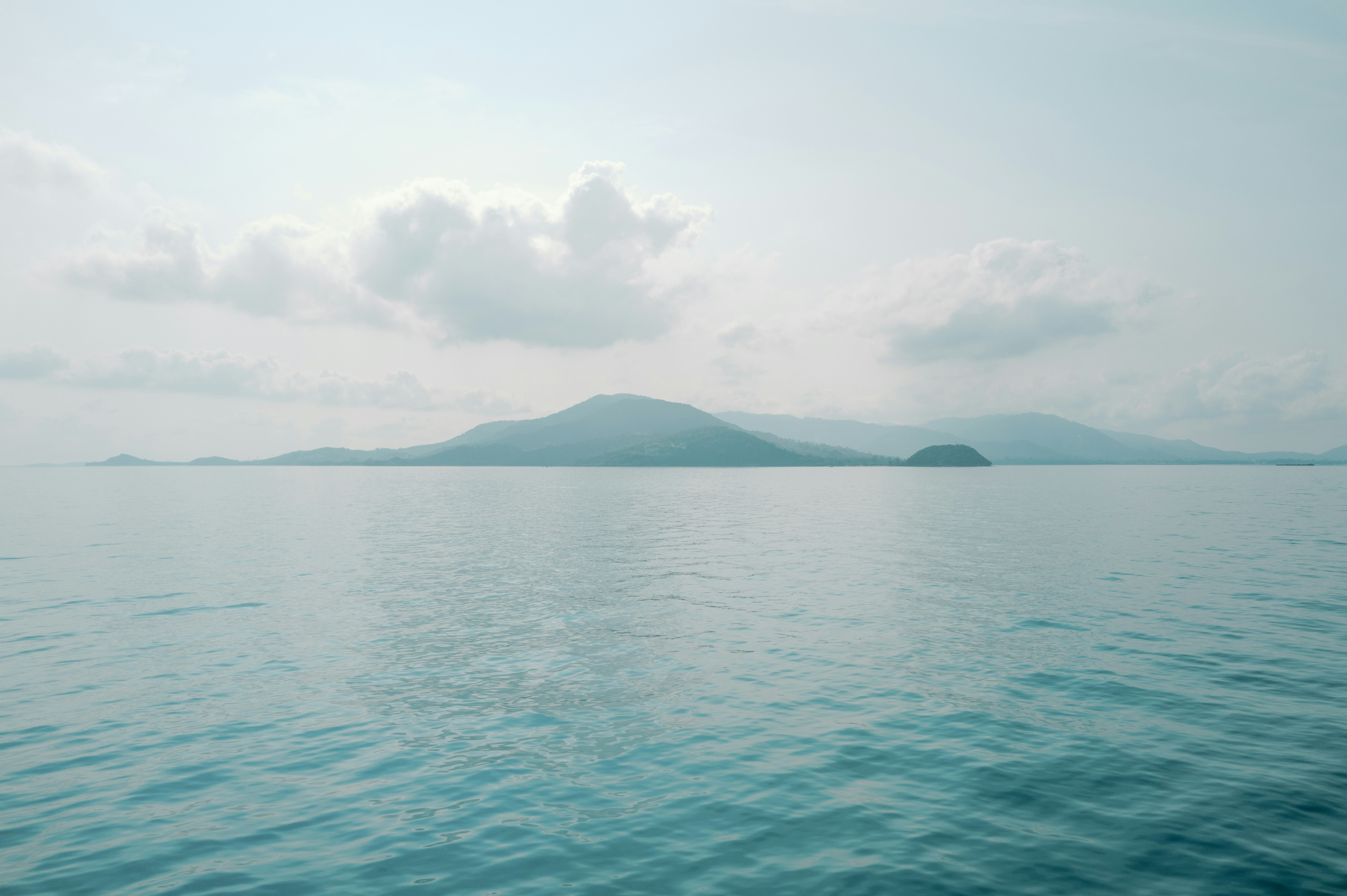 Calm ocean meets islands under a cloudy sky.