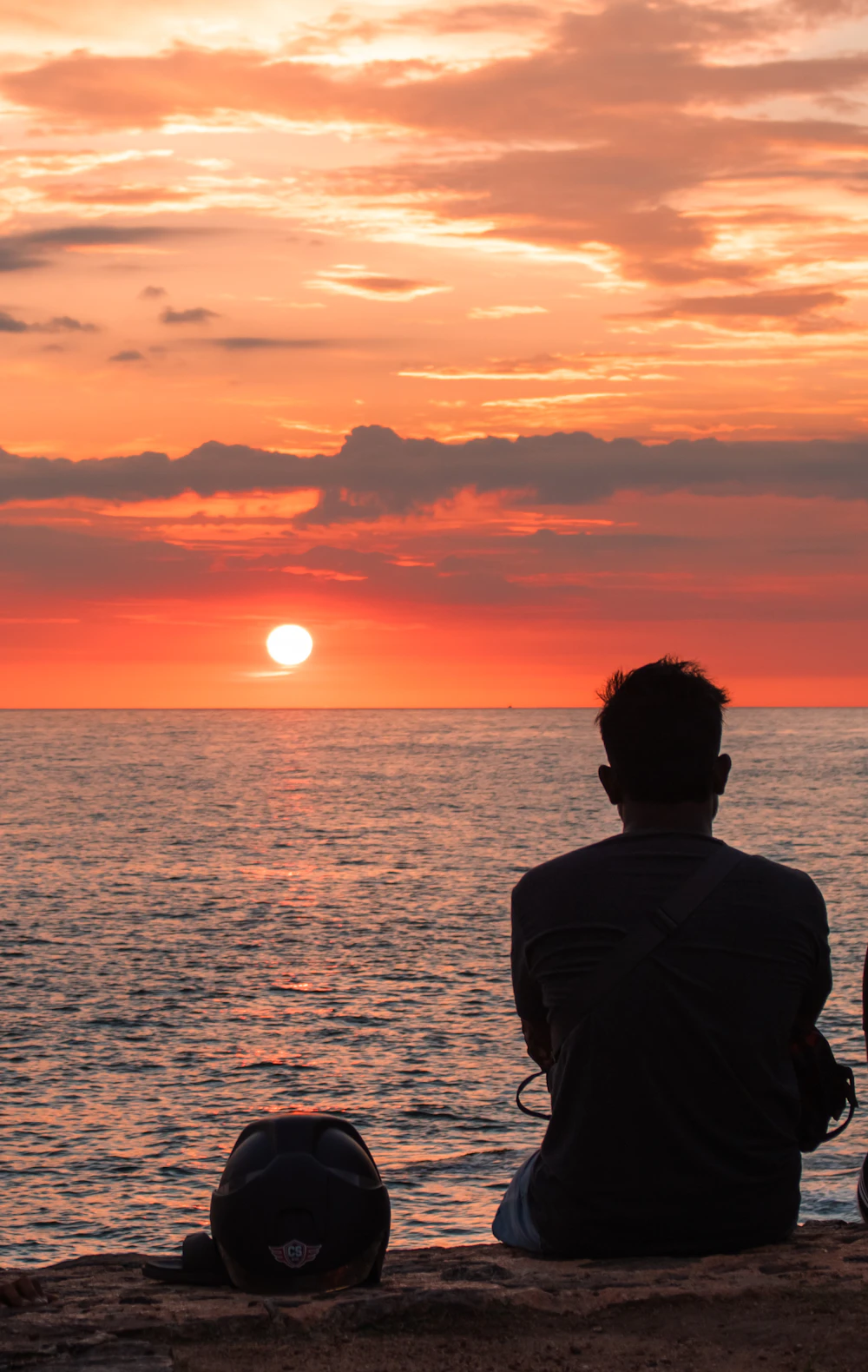A person sitting peacefully overlooking the ocean at sunset