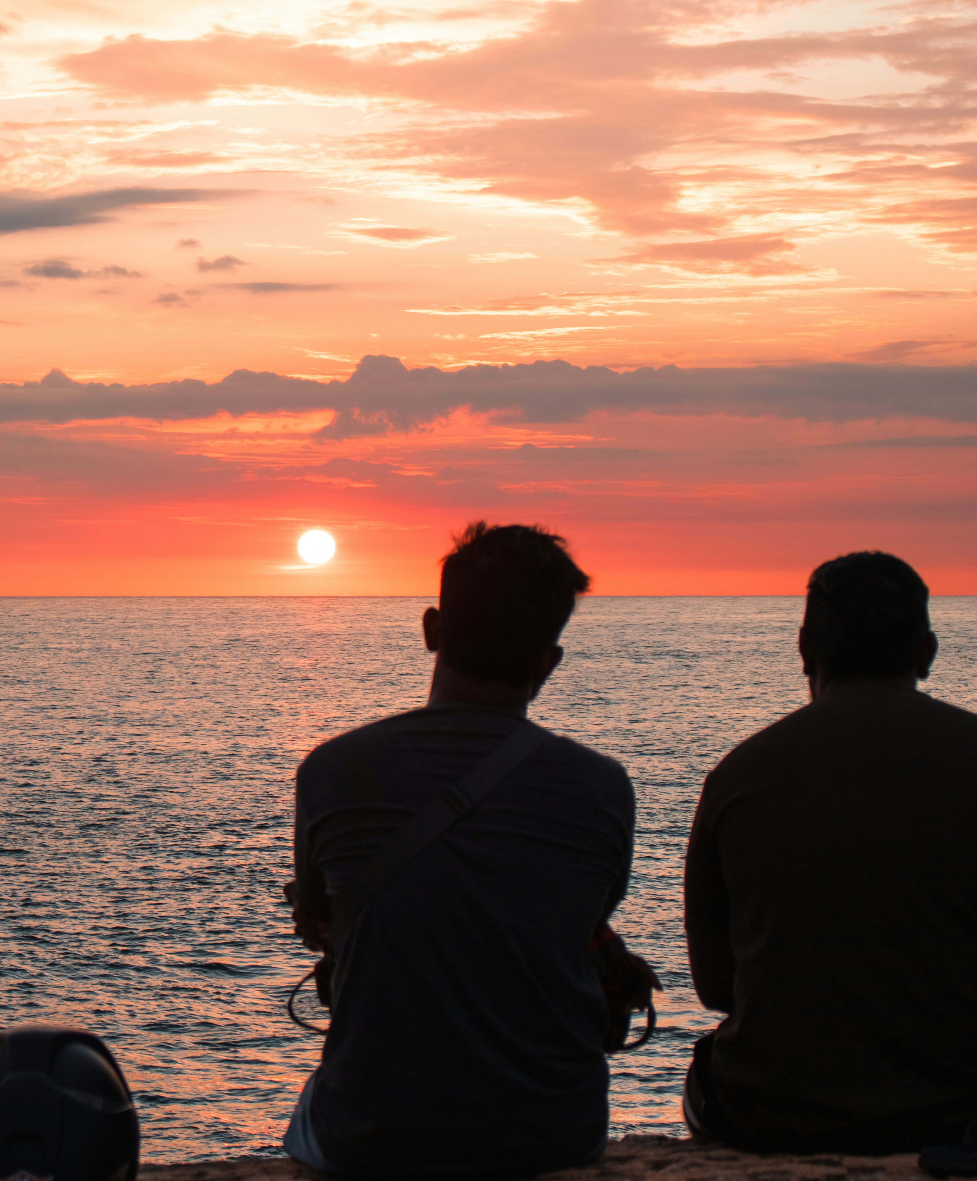Two figures watch the sunset over the ocean.