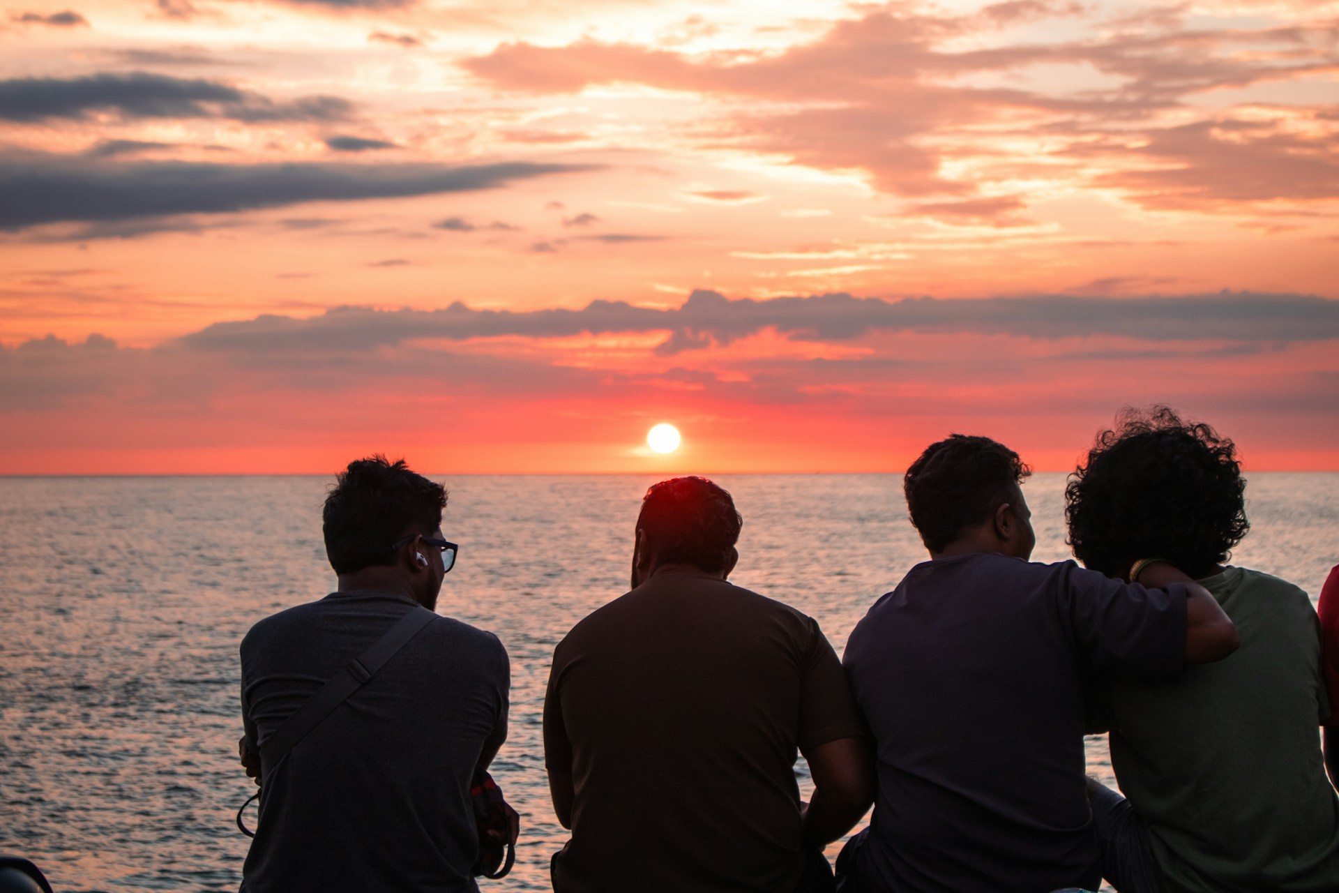 Friends watch a beautiful sunset over the ocean.
