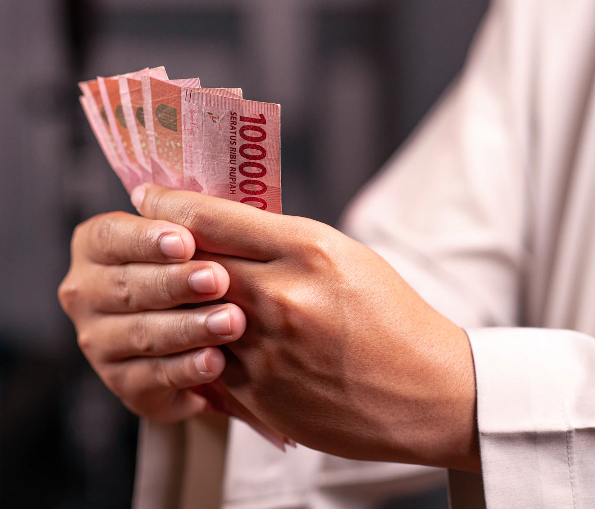 Dua tangan menghitung segebar uang kertas rupiah pecahan seratus ribu rupiah