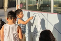Children are drawing on a white wall with a paintbrush.