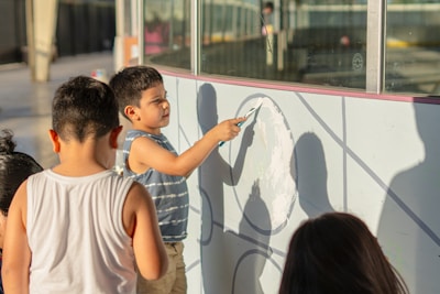 Children are drawing on a white wall with a paintbrush.