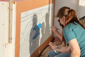 A woman paints a mural of silhouetted figures.