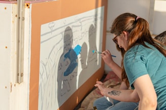 A woman paints a mural of silhouetted figures.