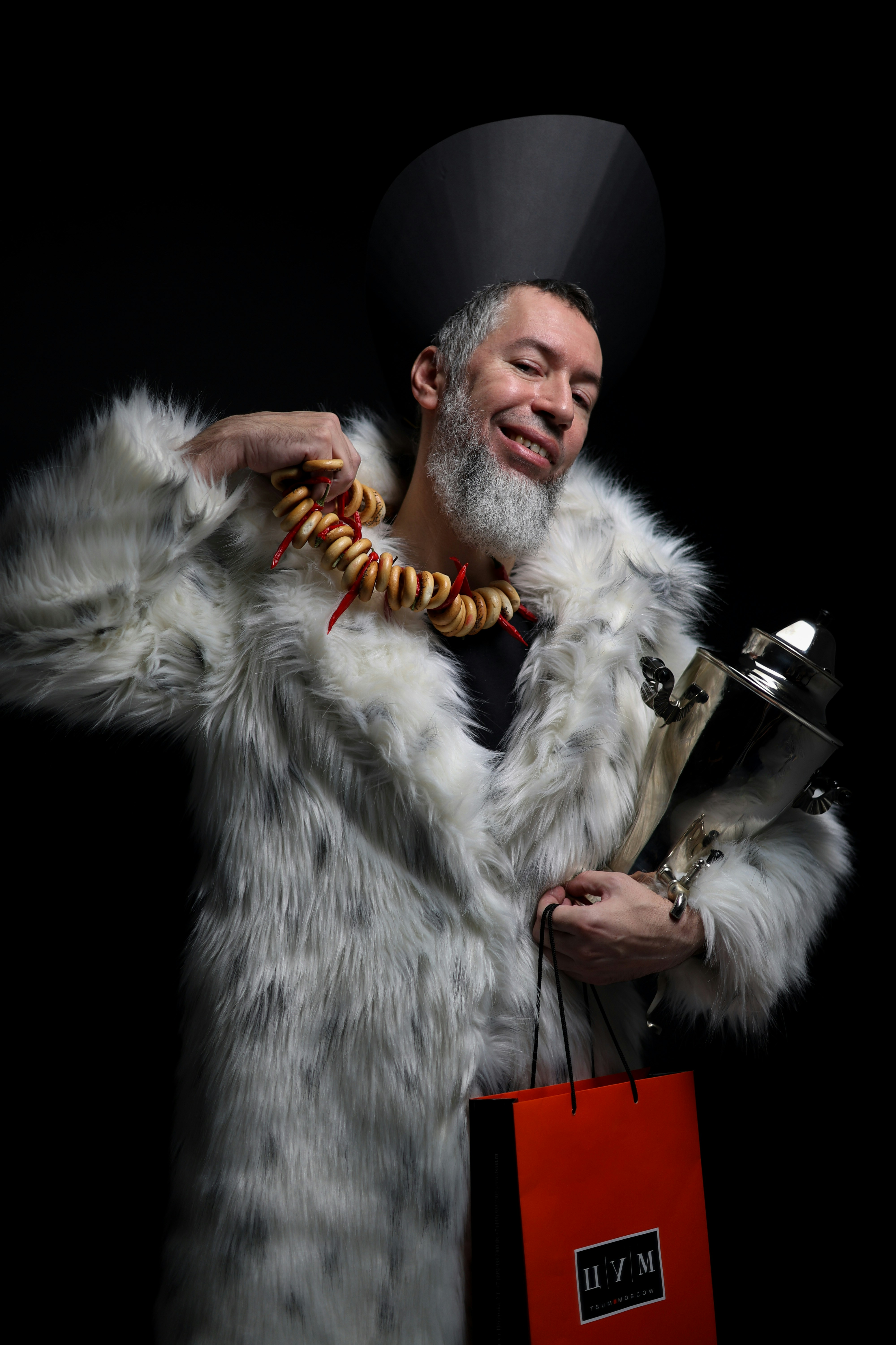 A man smiles wearing a coat with a bagel necklace.