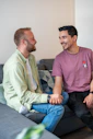 Two men smile and chat on a couch.