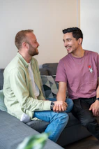 Two men smile and chat on a couch.