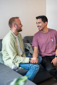 Two men smile and chat on a couch.