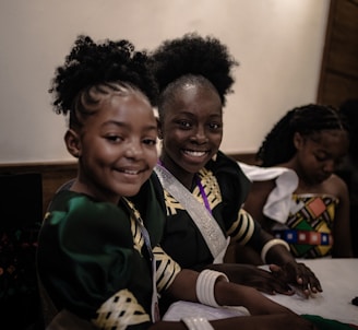 Three smiling girls are dressed in cultural attire.