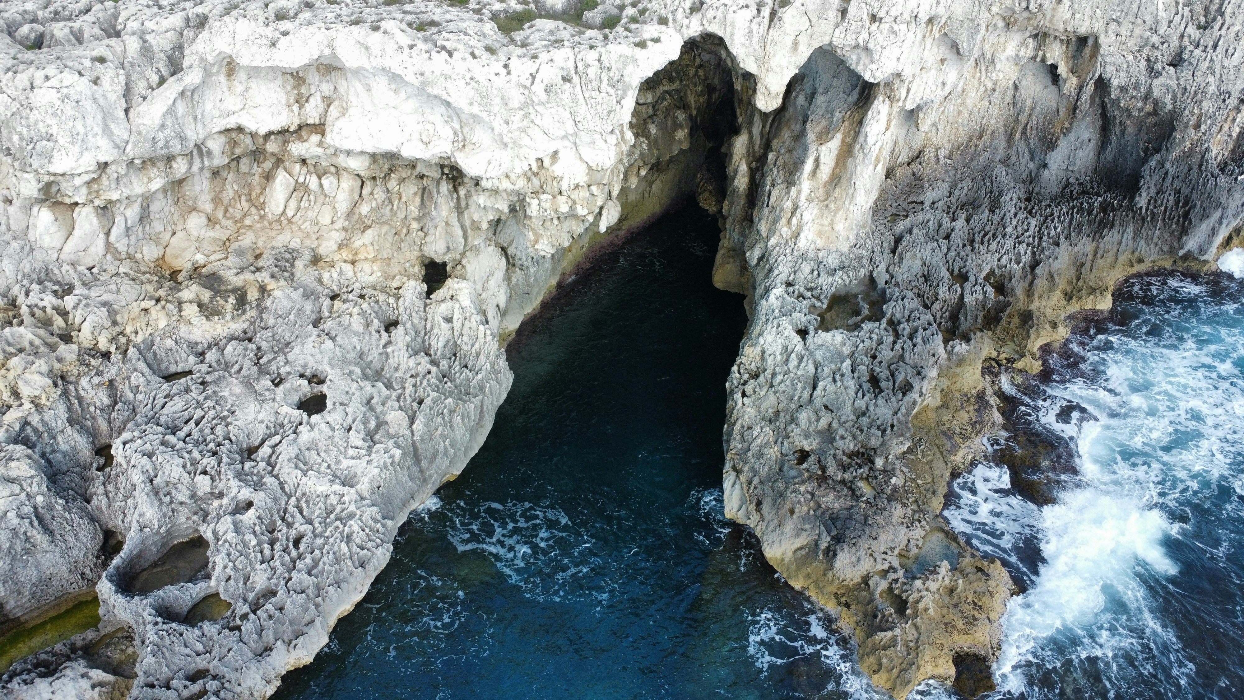 Cliffside cave entrance with deep blue water.