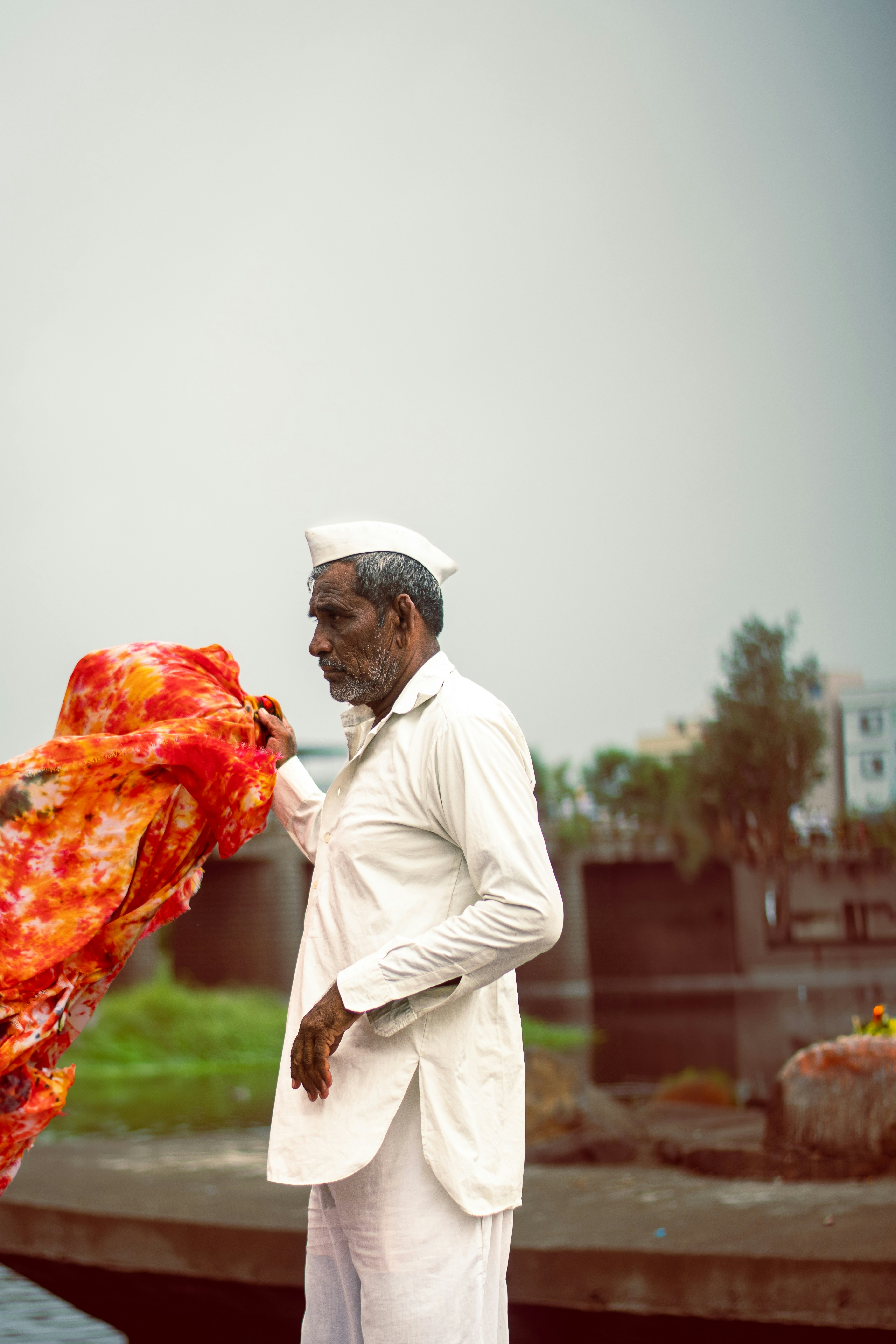 An elderly man stands outdoors holding fabric.