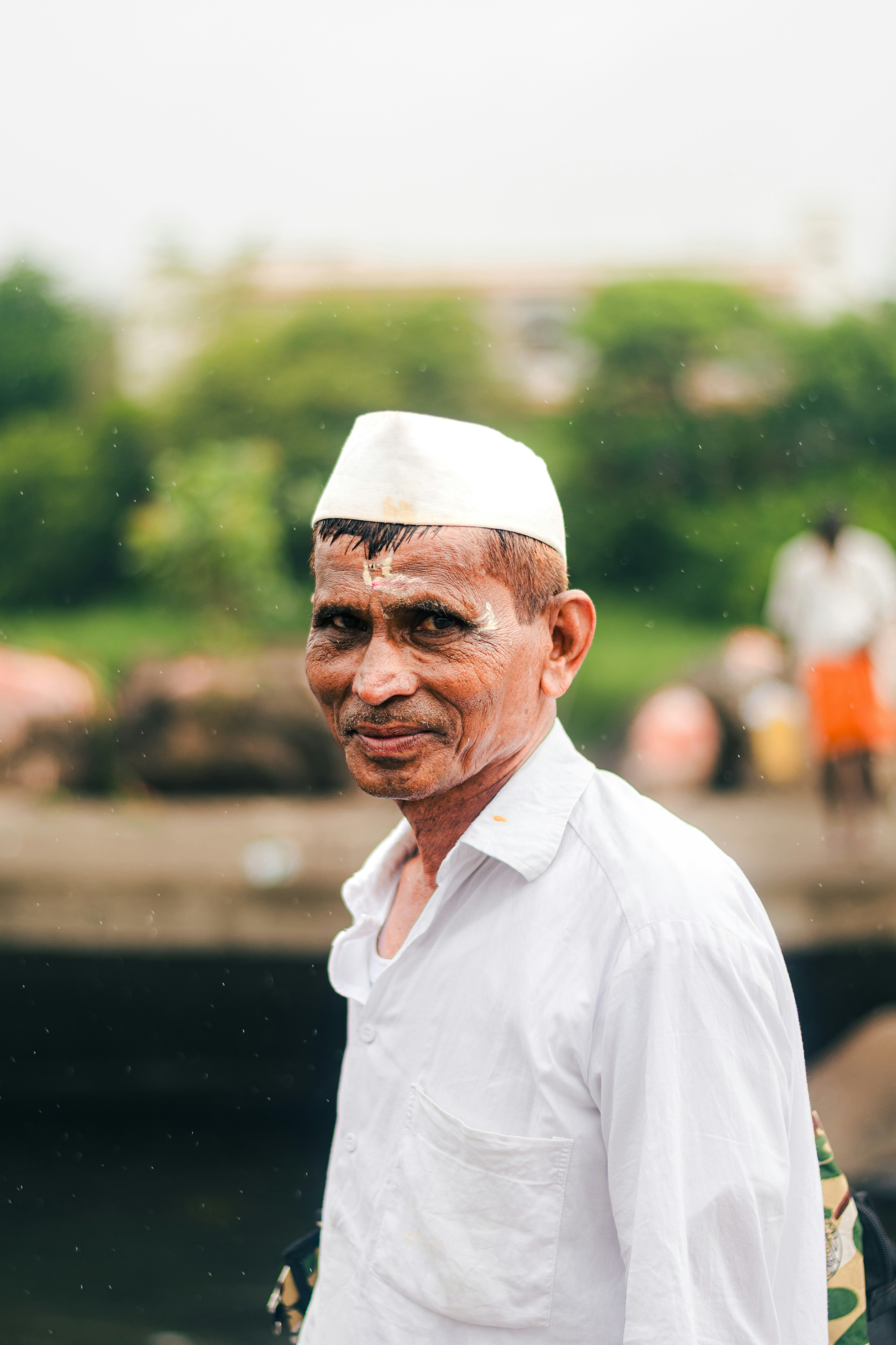 An elderly indian man in a white outfit smiles.