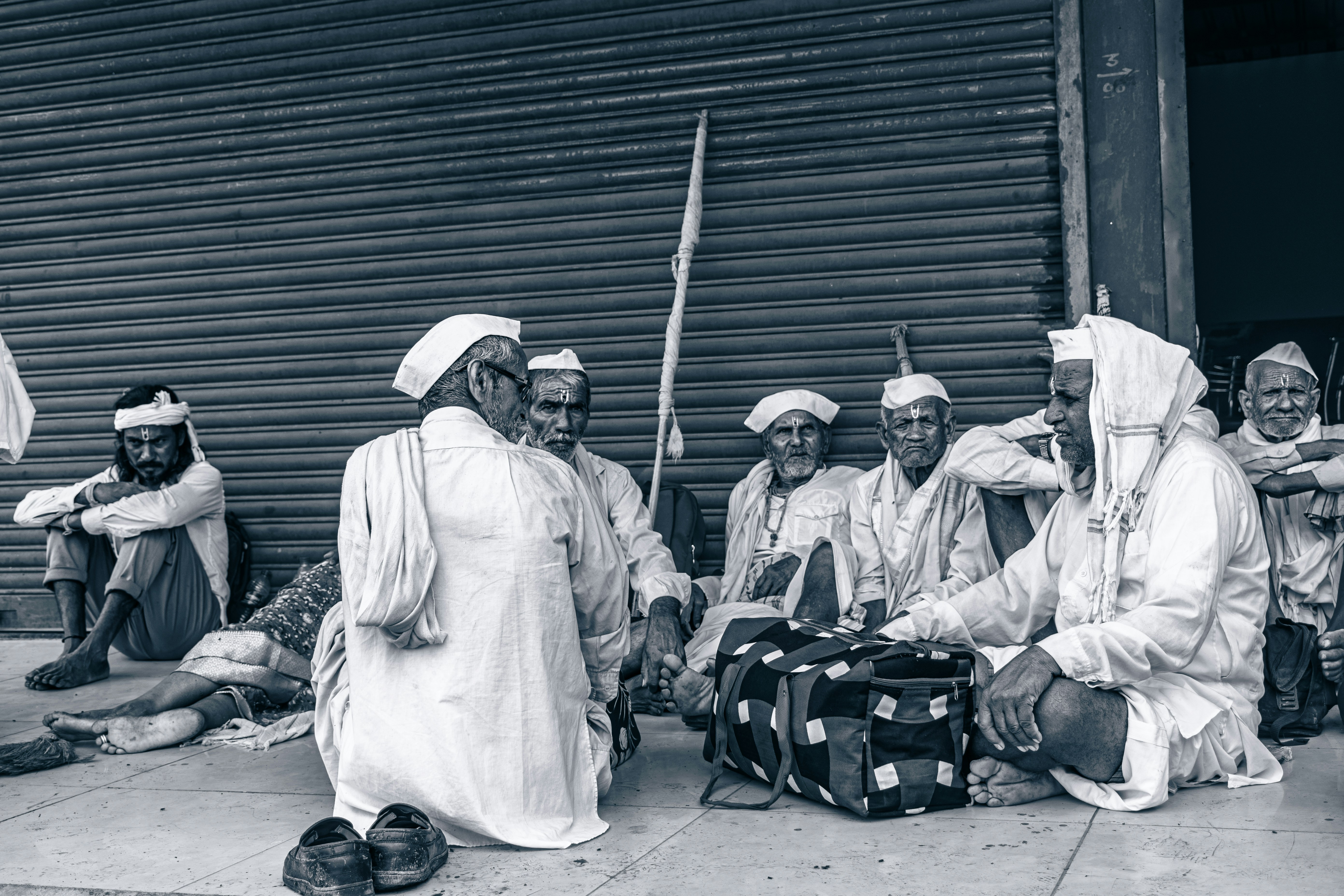 Men wearing white clothing sit together outside.