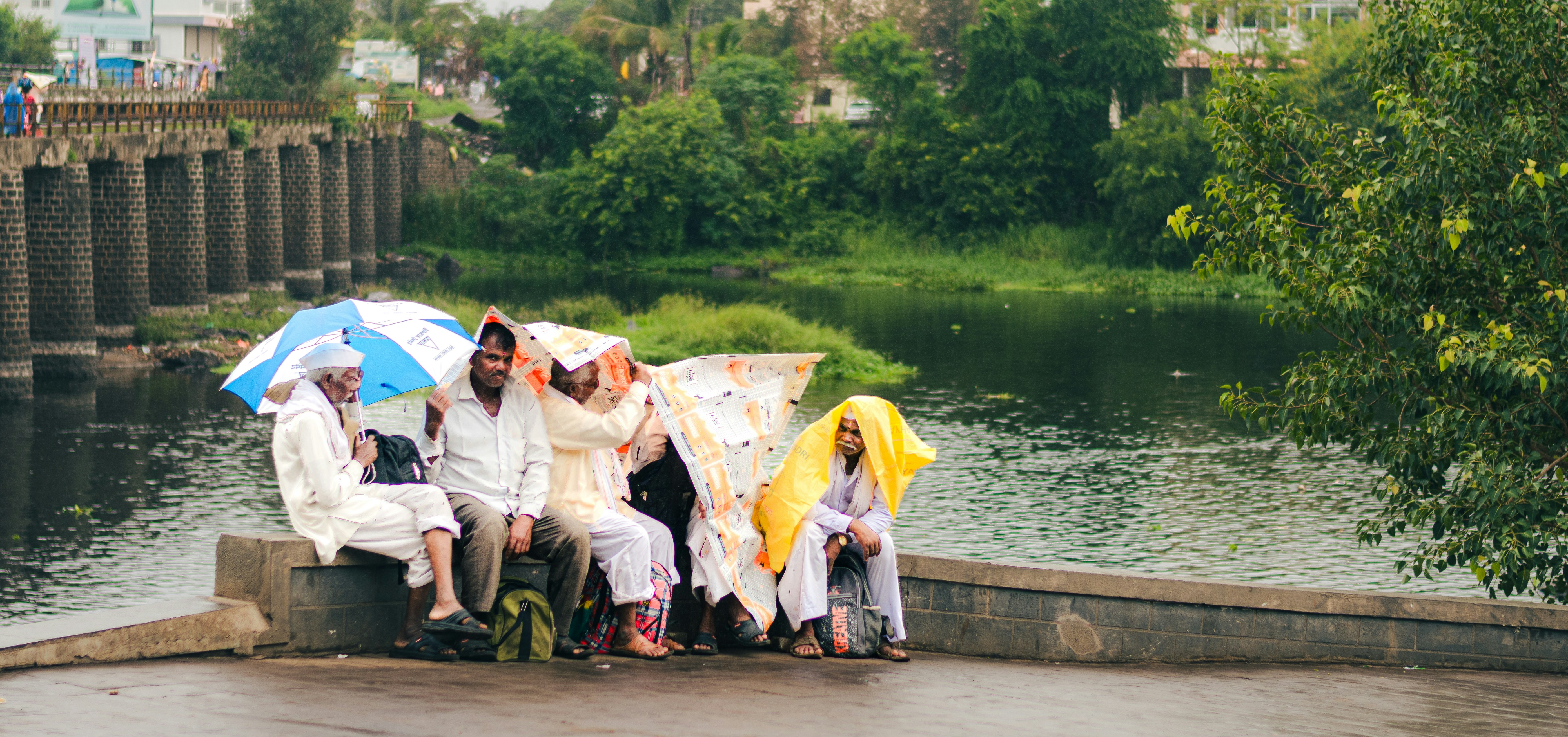 People shelter from the rain near a bridge and water.