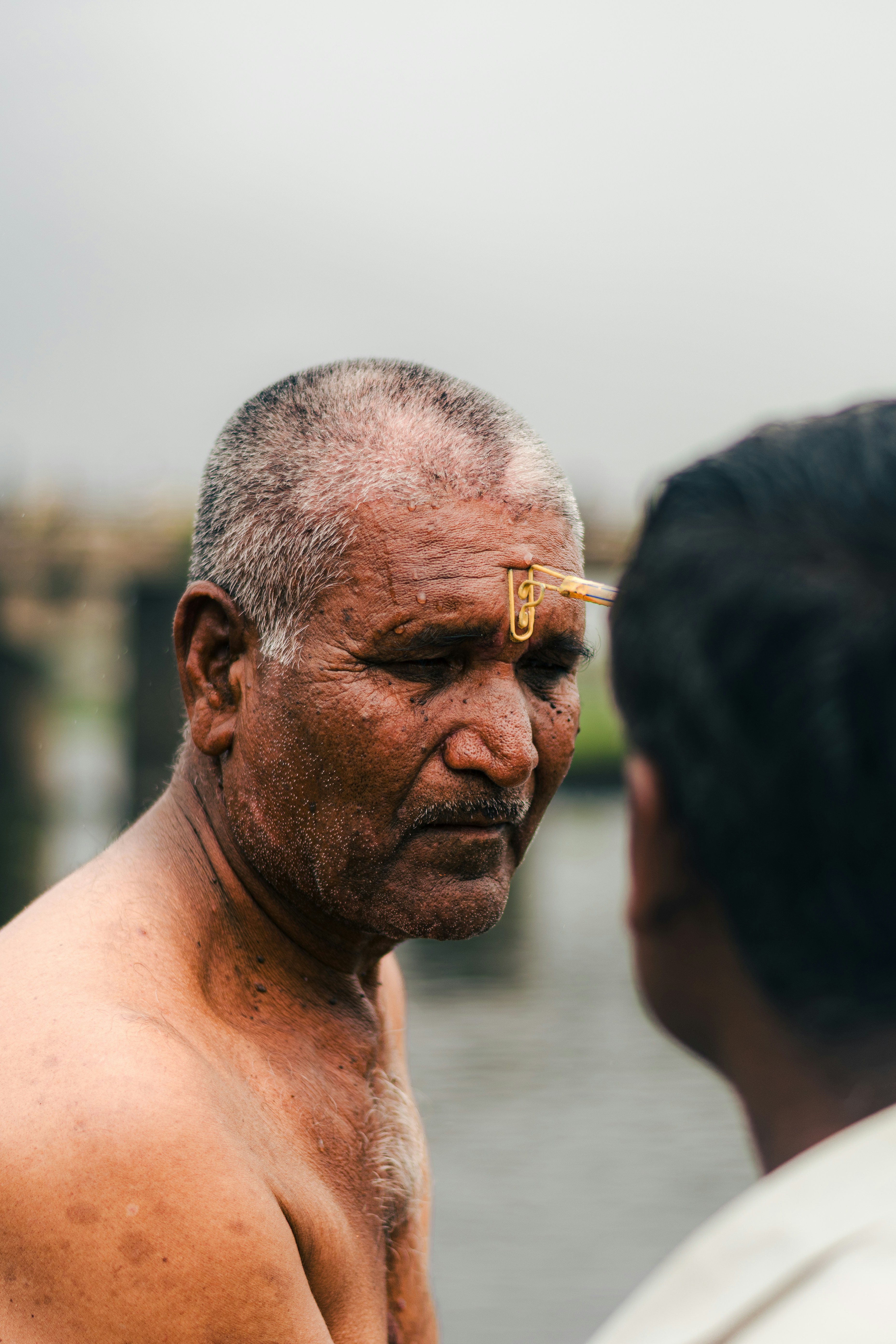 An older man with a bindi talks to another.