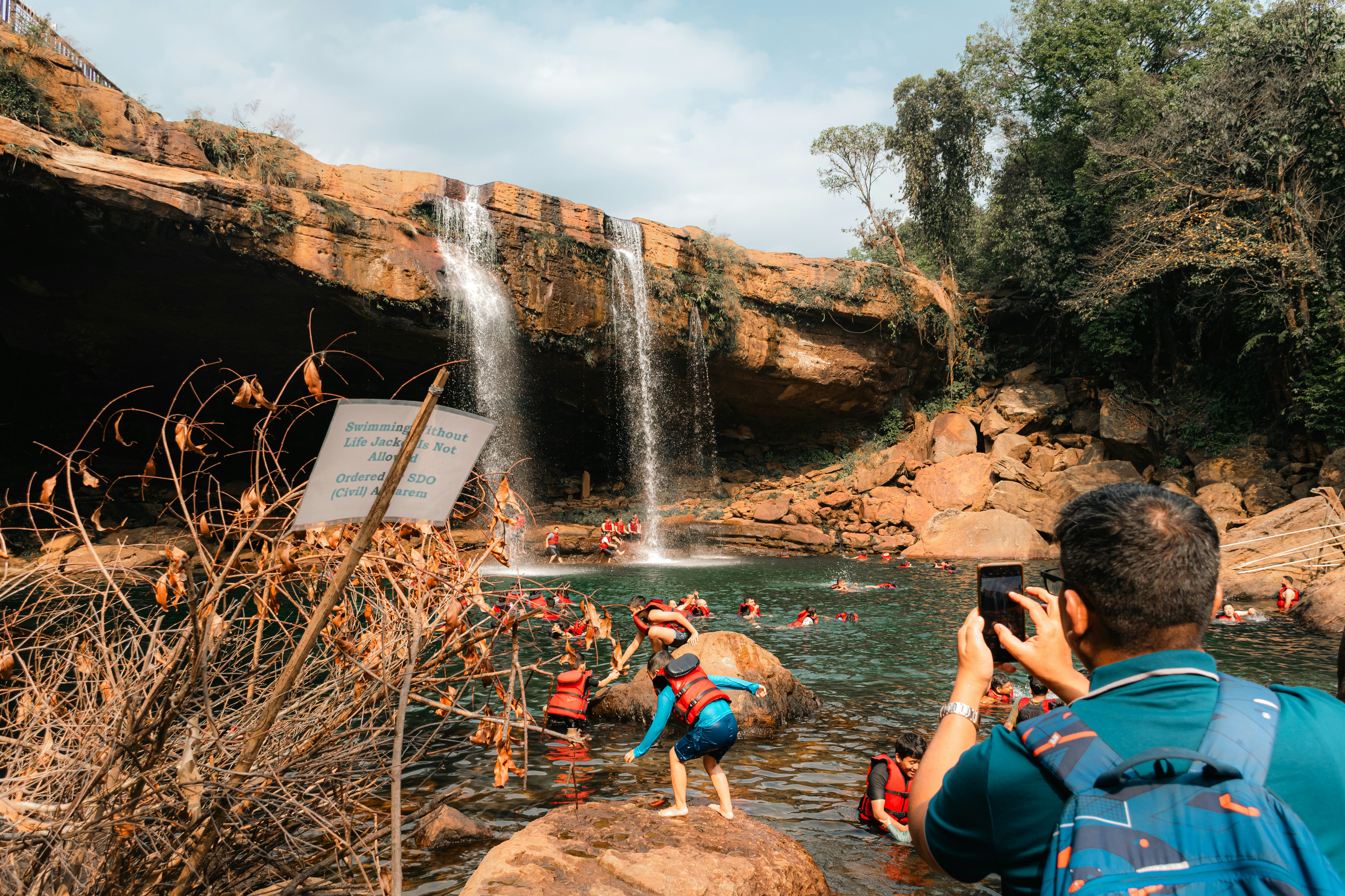 People swim and enjoy underneath a beautiful waterfall.