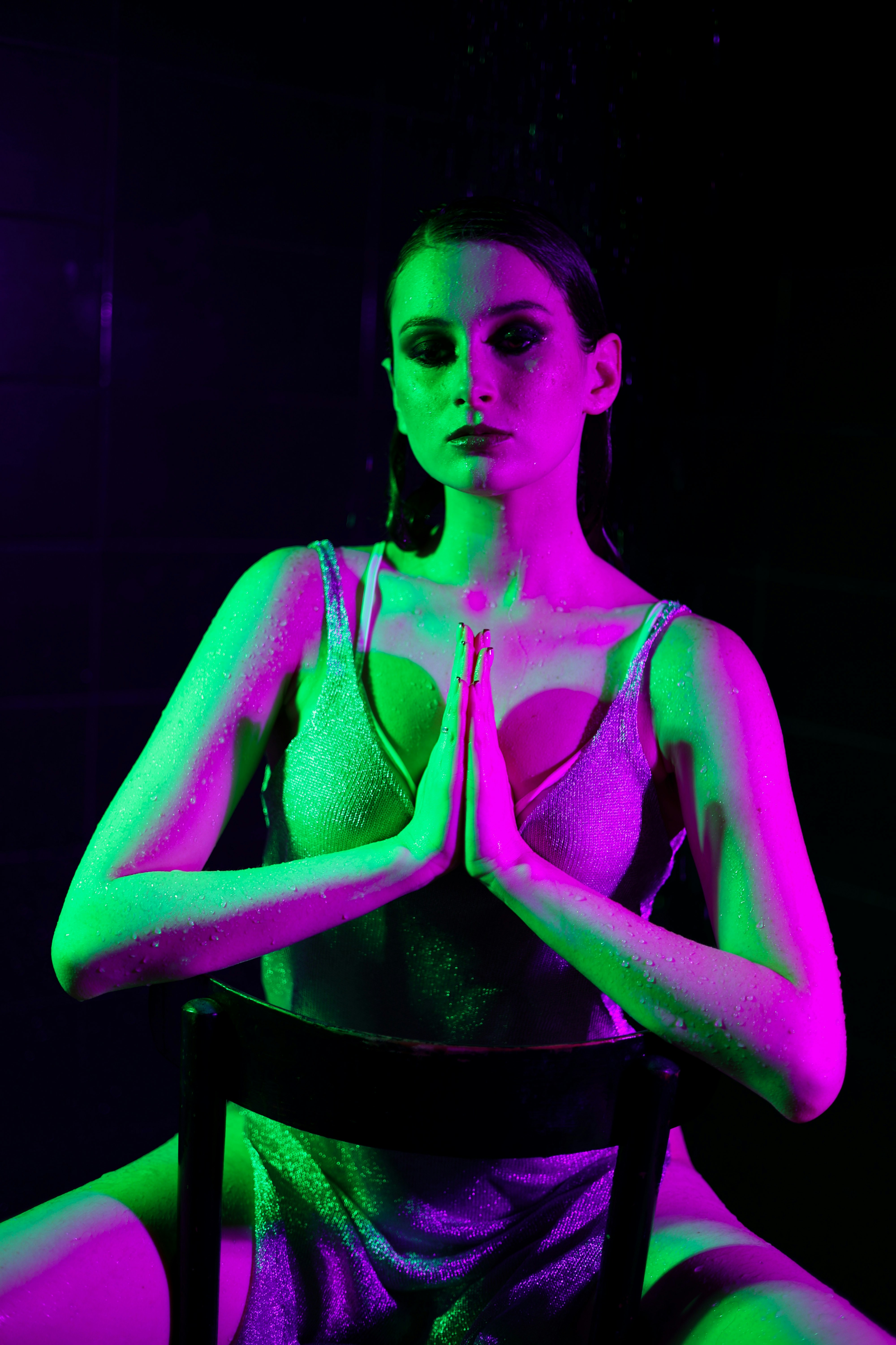 Woman in neon lights sits with hands clasped.