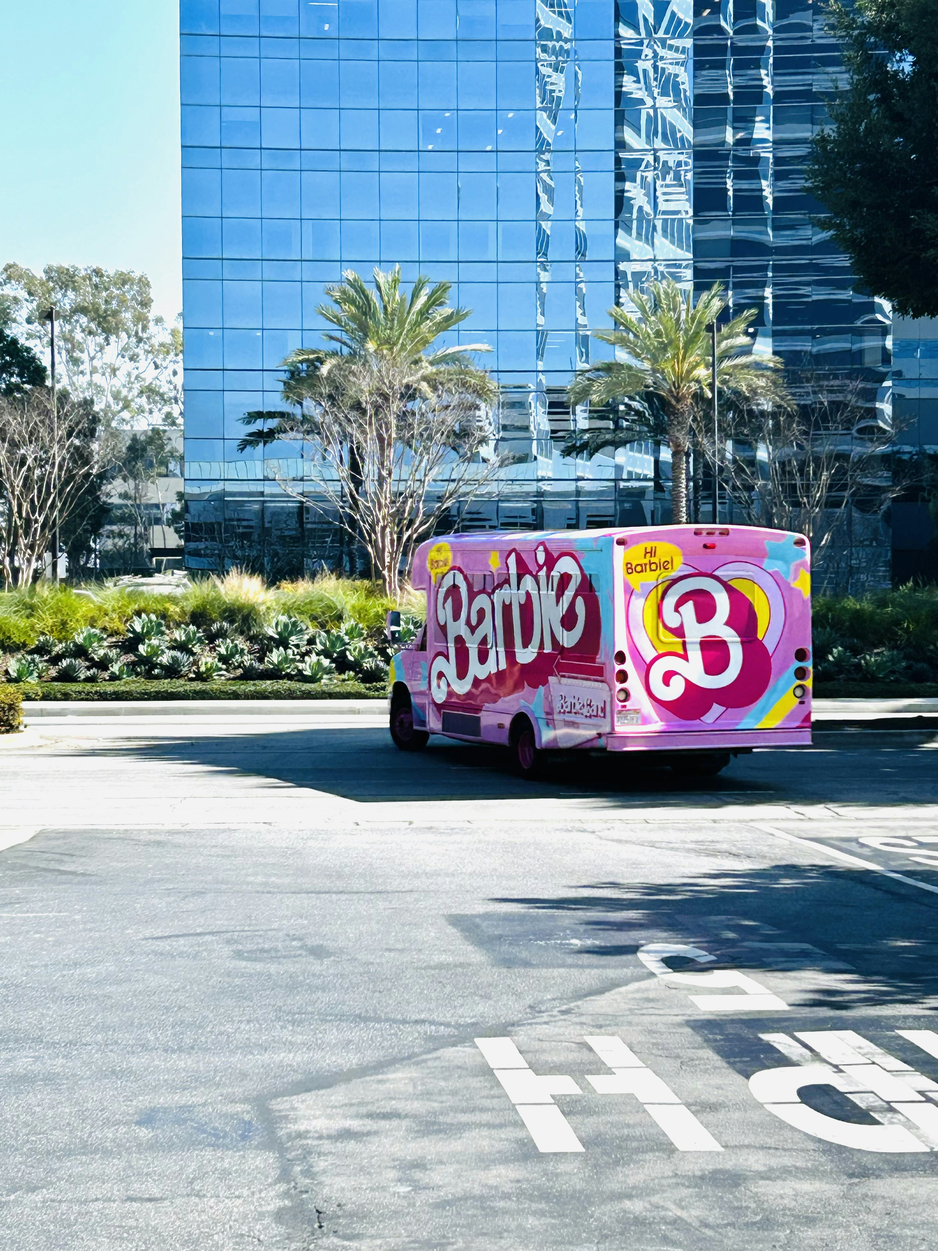 A pink barbie truck is parked in front of a building.