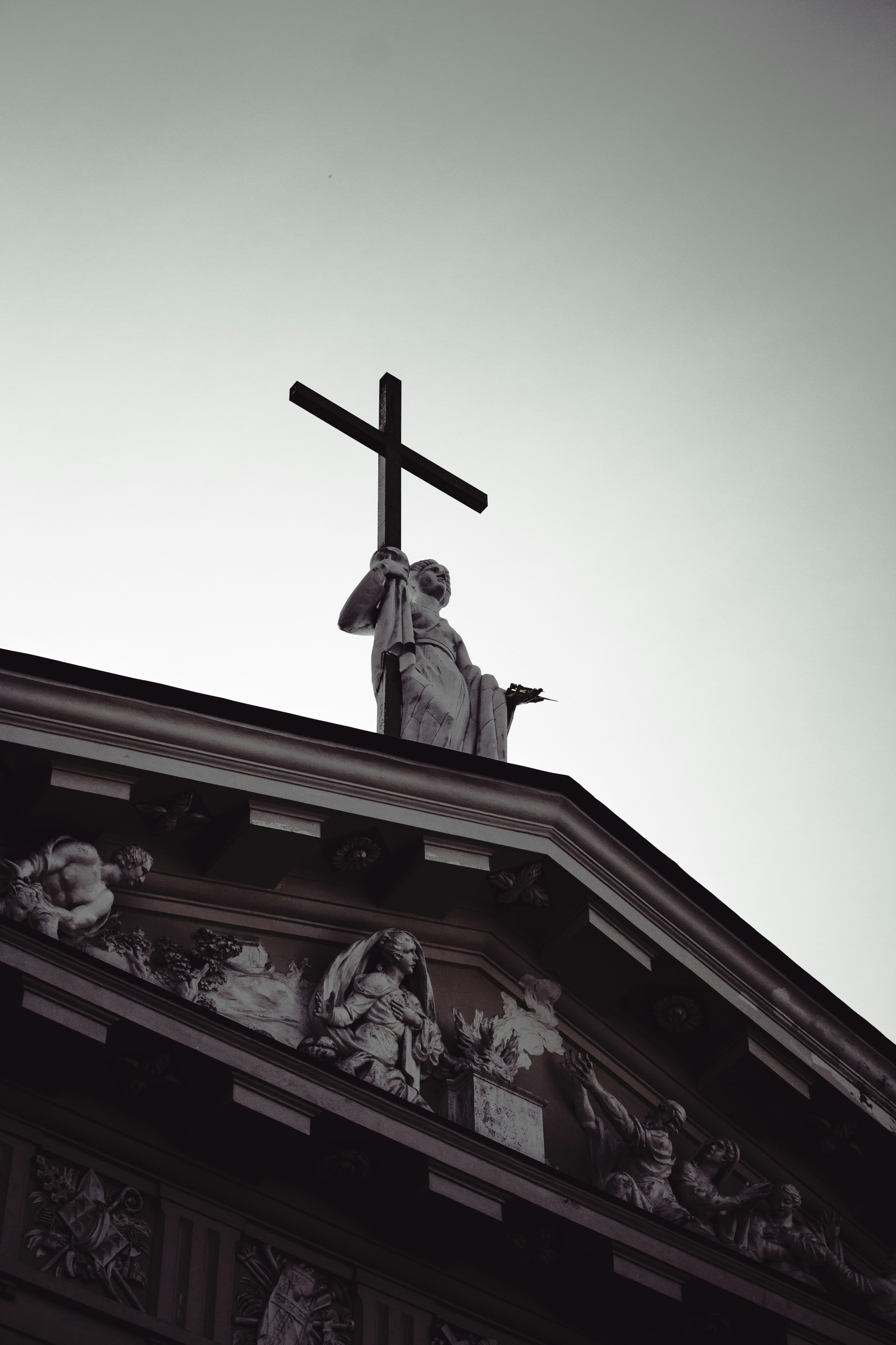 Statue holds a cross atop a church.