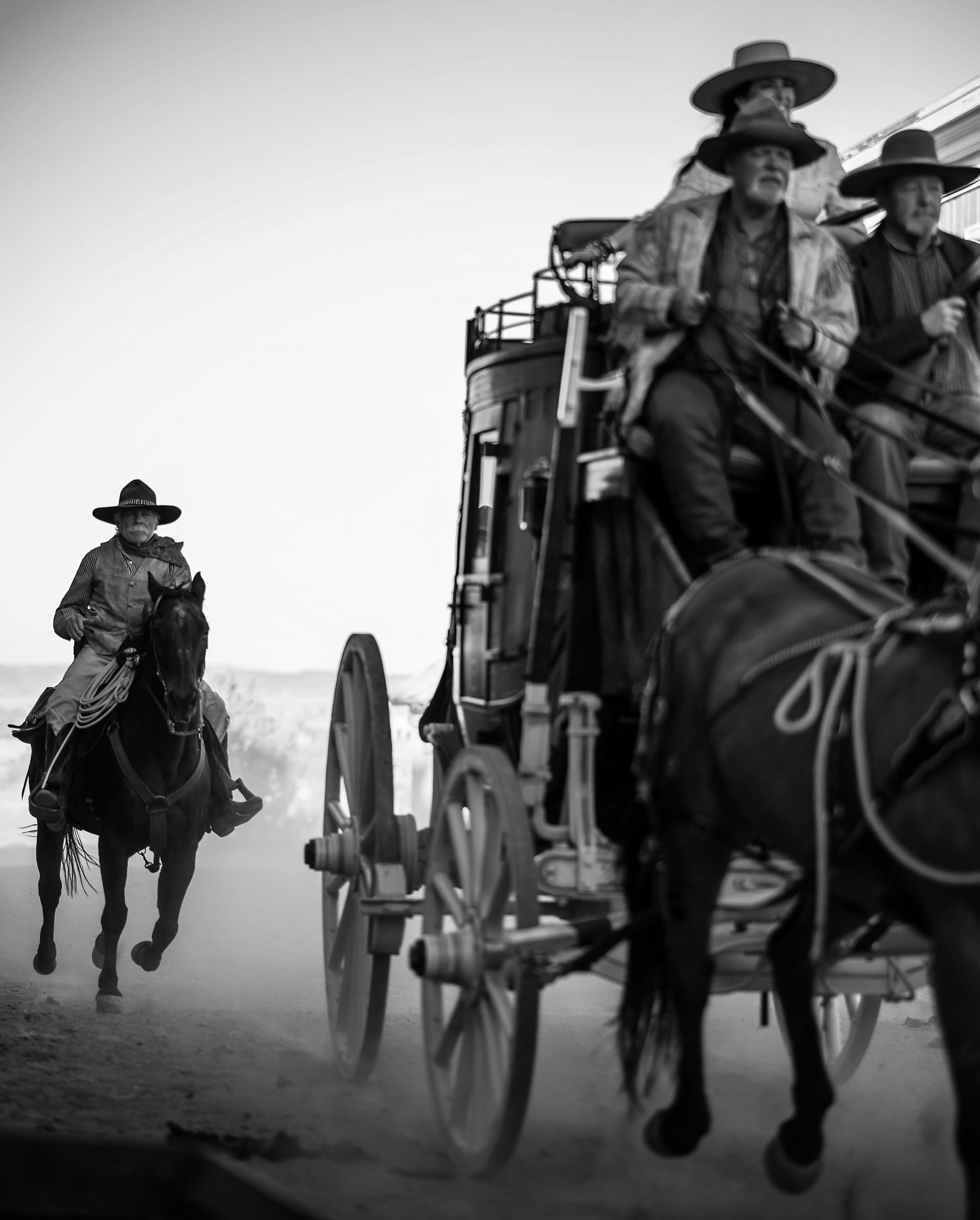 Cowboys ride horses and a stagecoach travels.