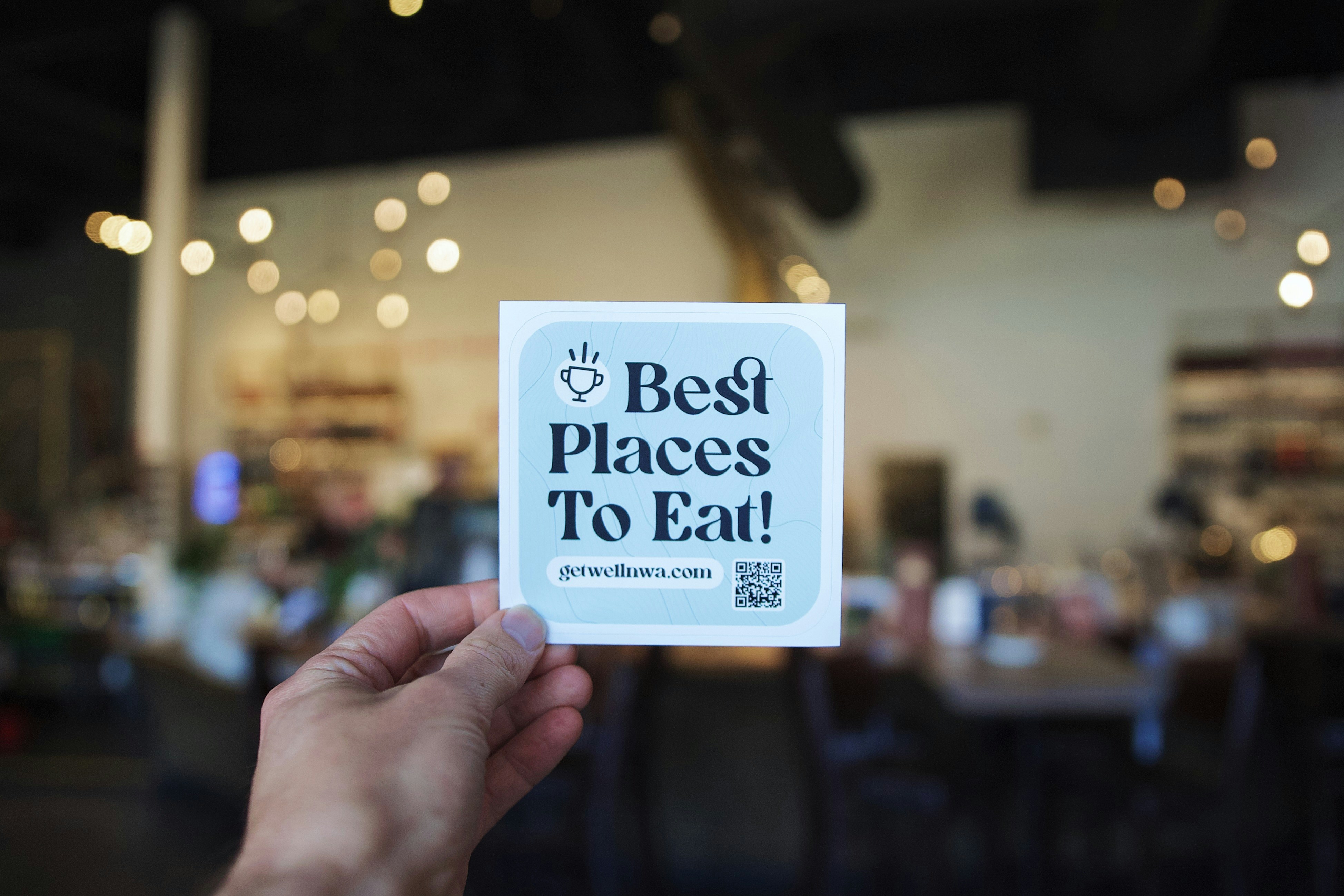 A hand holds a "best places to eat" sign.