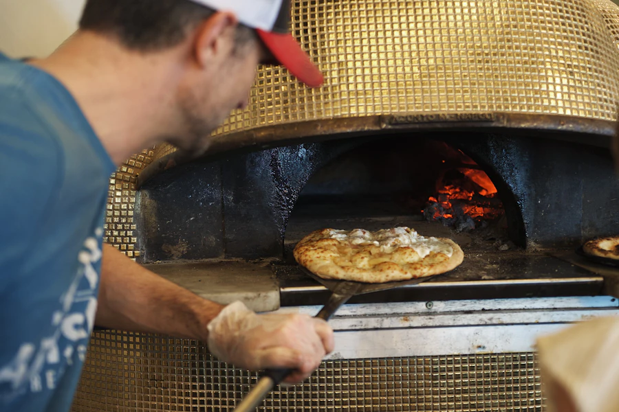 Pizzaiolo tirando a pizza do forno a lenha