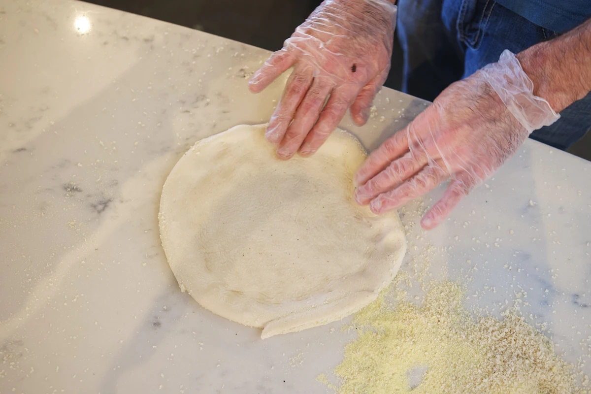 Hands stretching a pizza dough into a thin round shape, showing the dough's extensibility