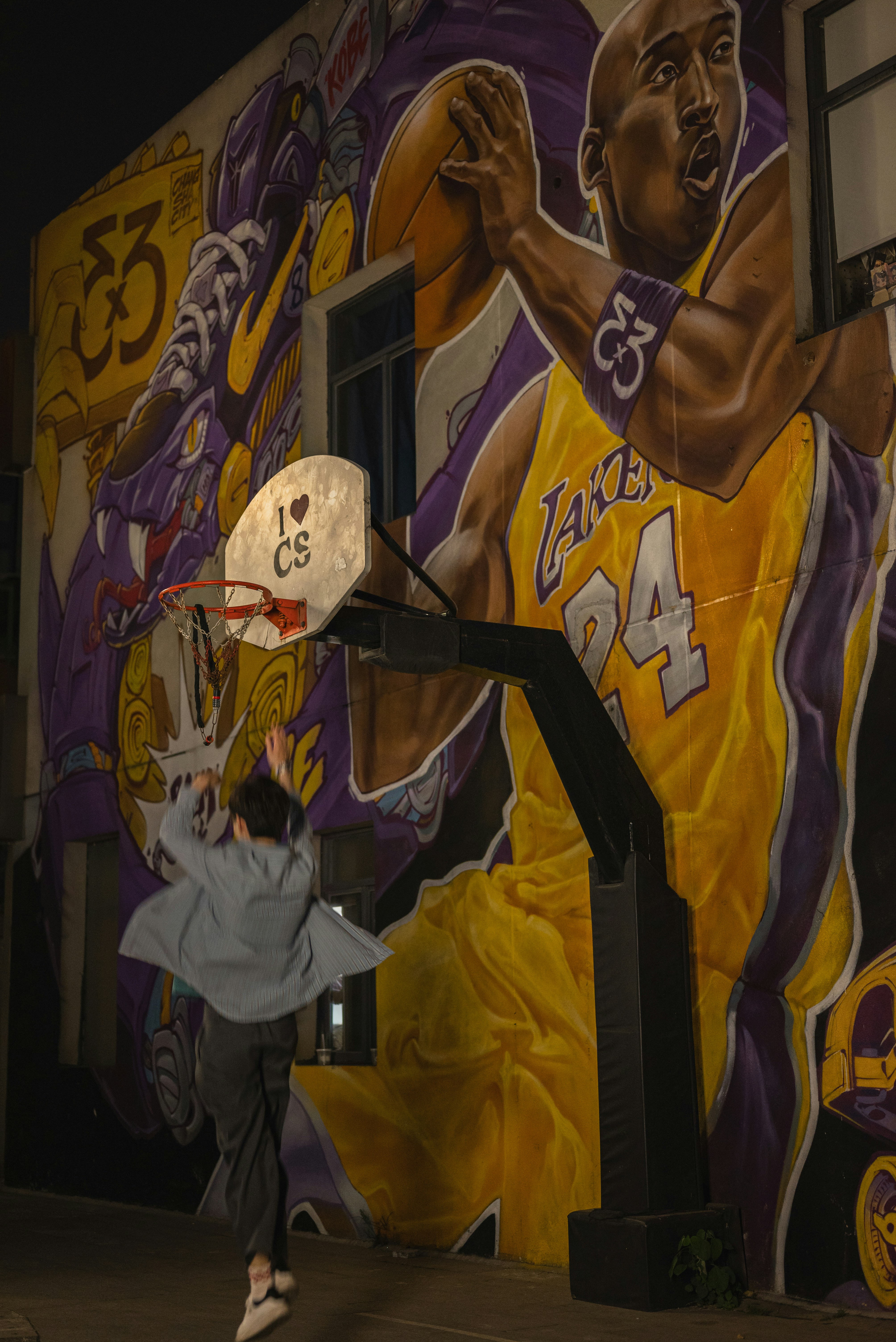 A person shoots a basketball with a mural backdrop.
