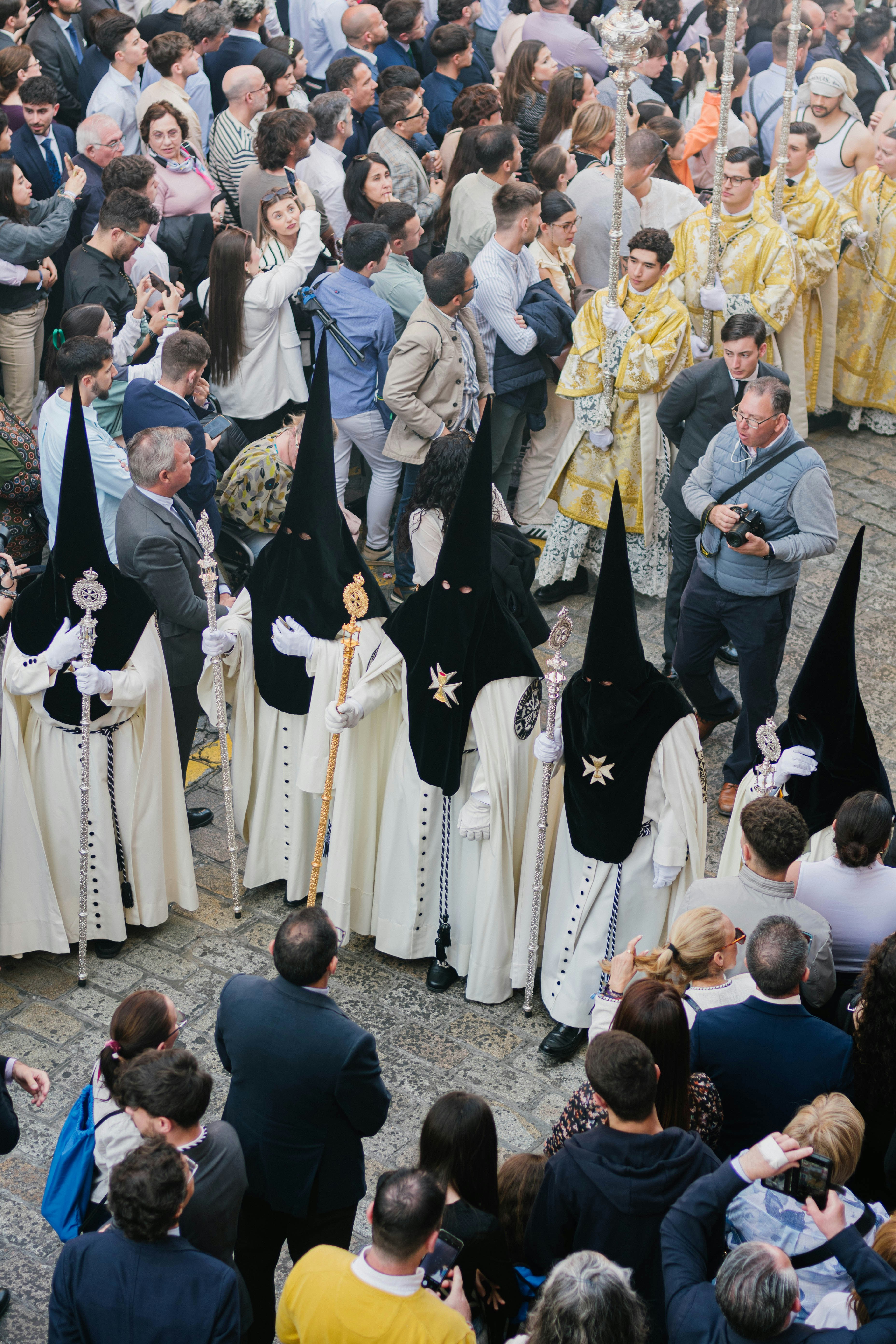 A religious procession features hooded figures and a crowd.