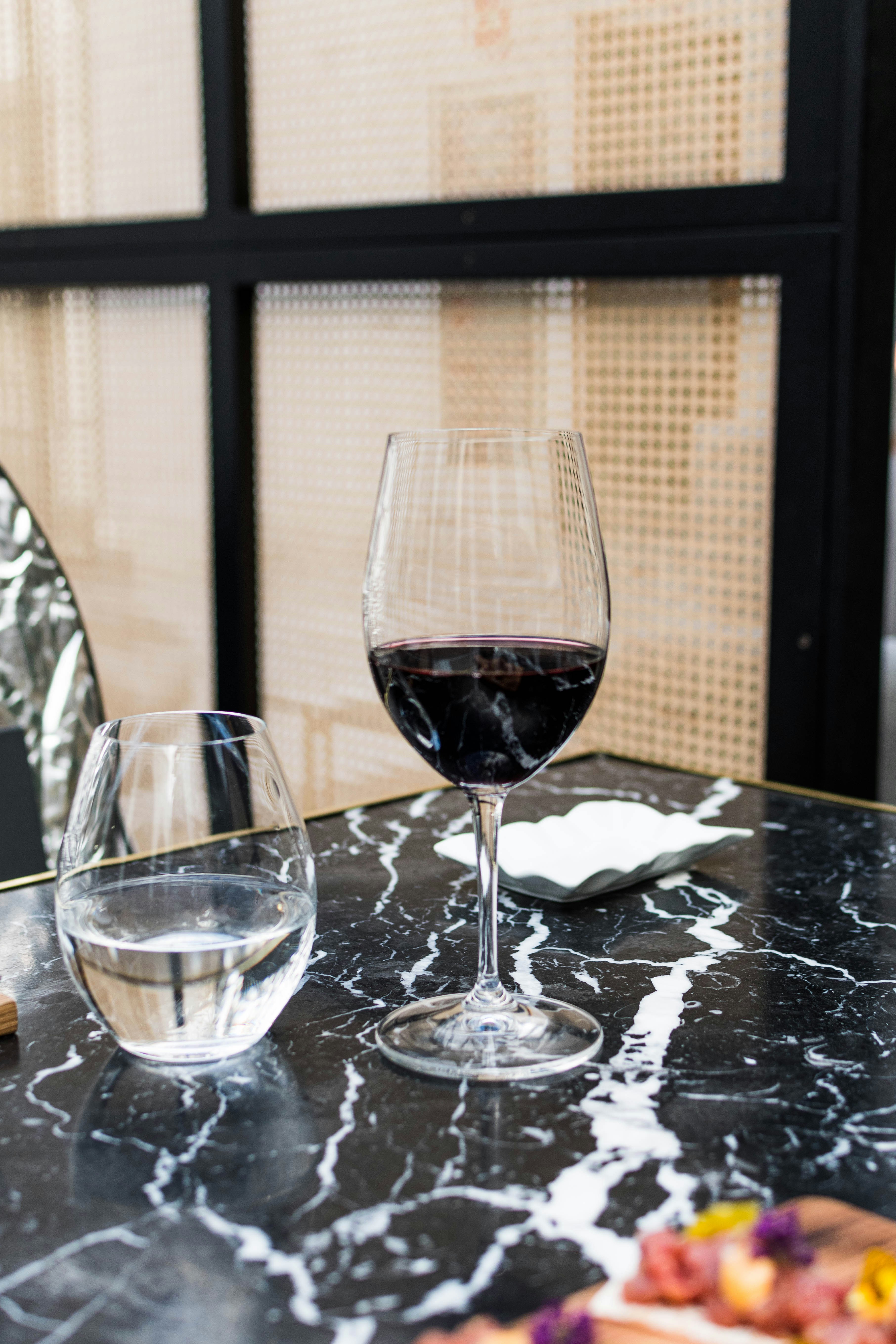 Red wine and water sit on a marbled table.