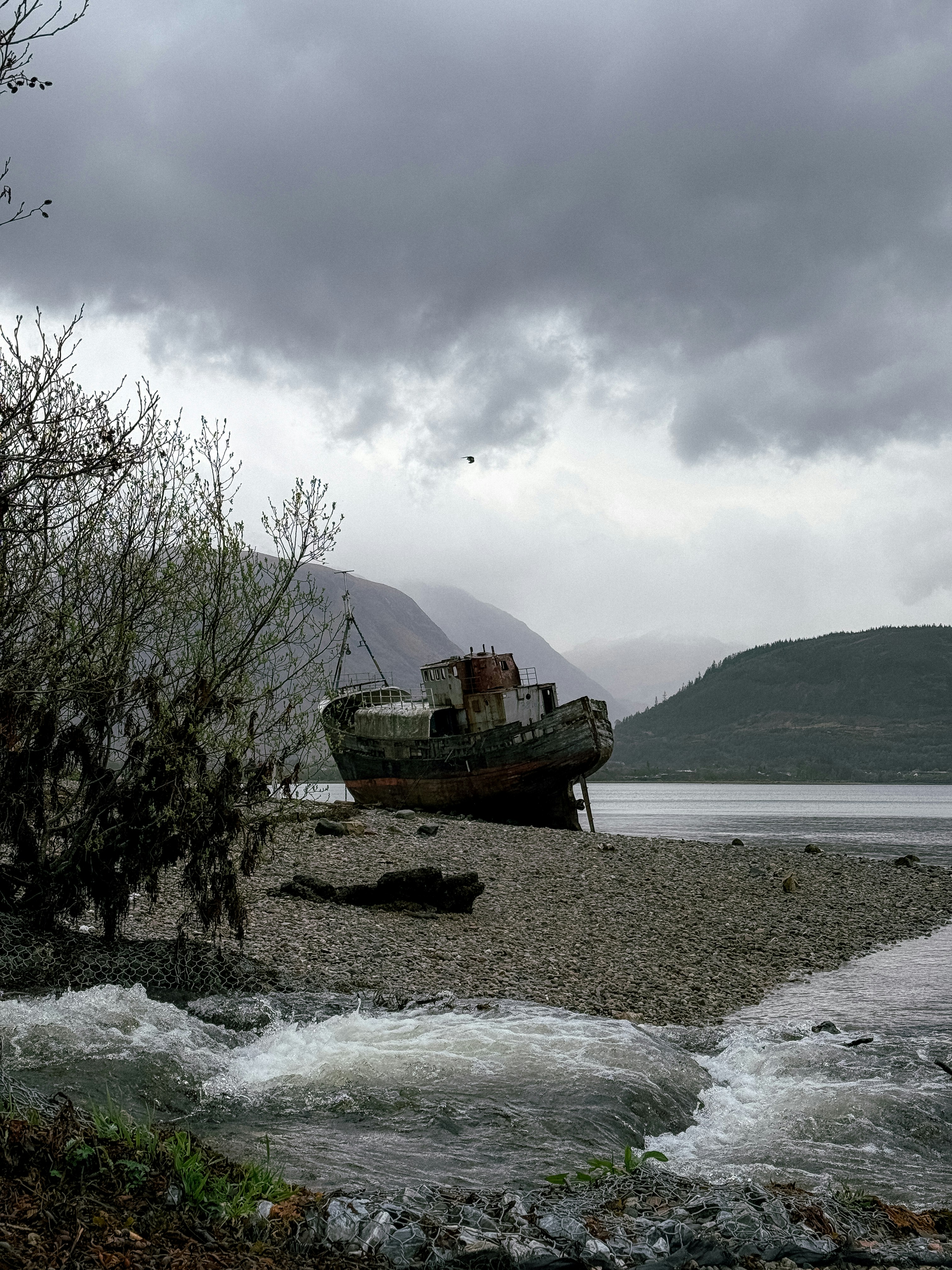 Weathered boat on shore under dramatic skies.