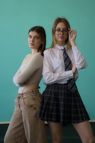 Two young women pose in front of a blue background.