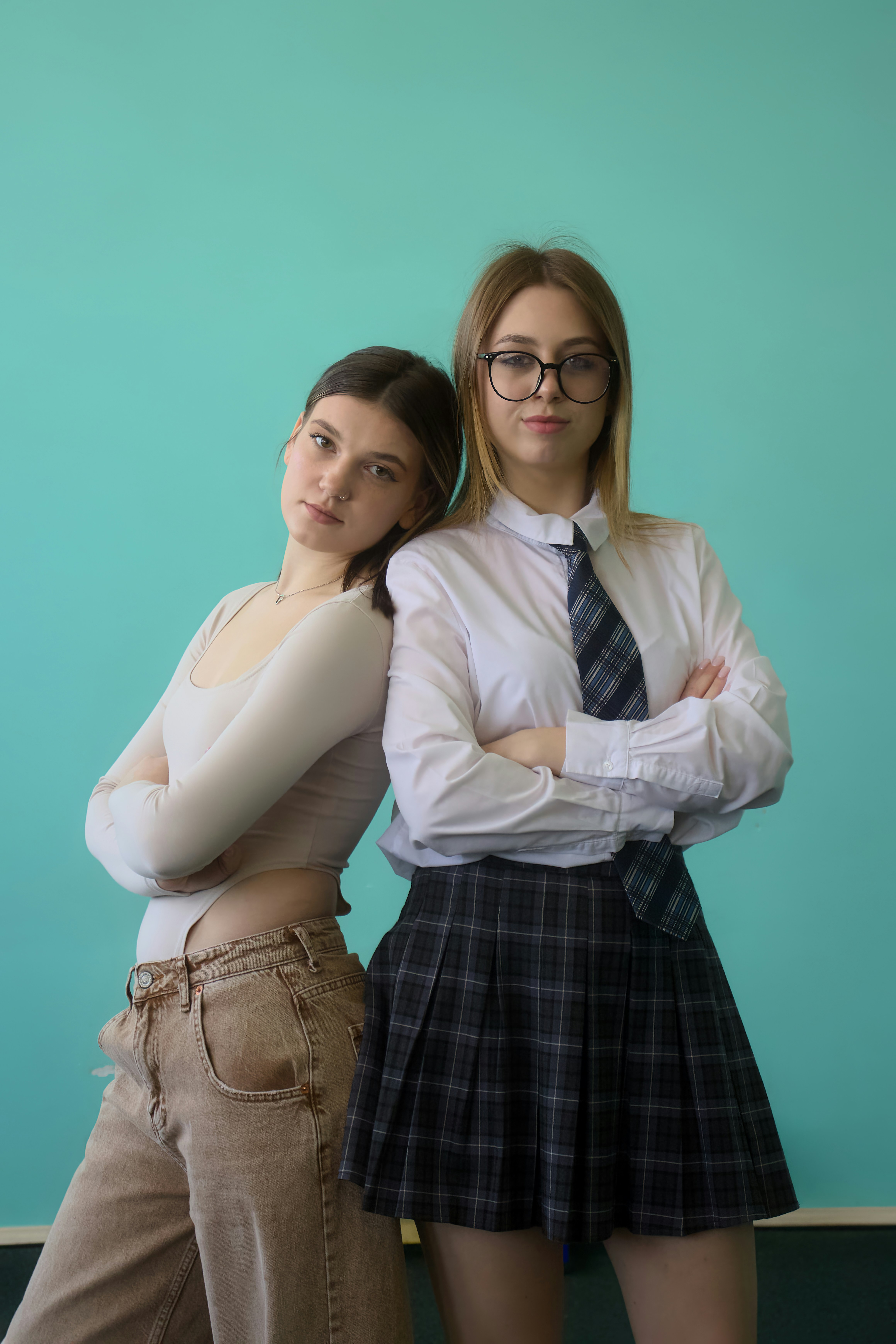 Two young women stand together against a blue wall.