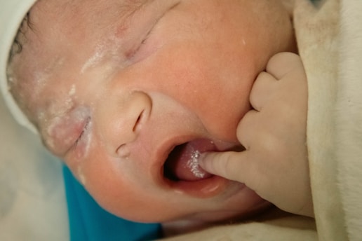 A newborn baby has a finger in its mouth.