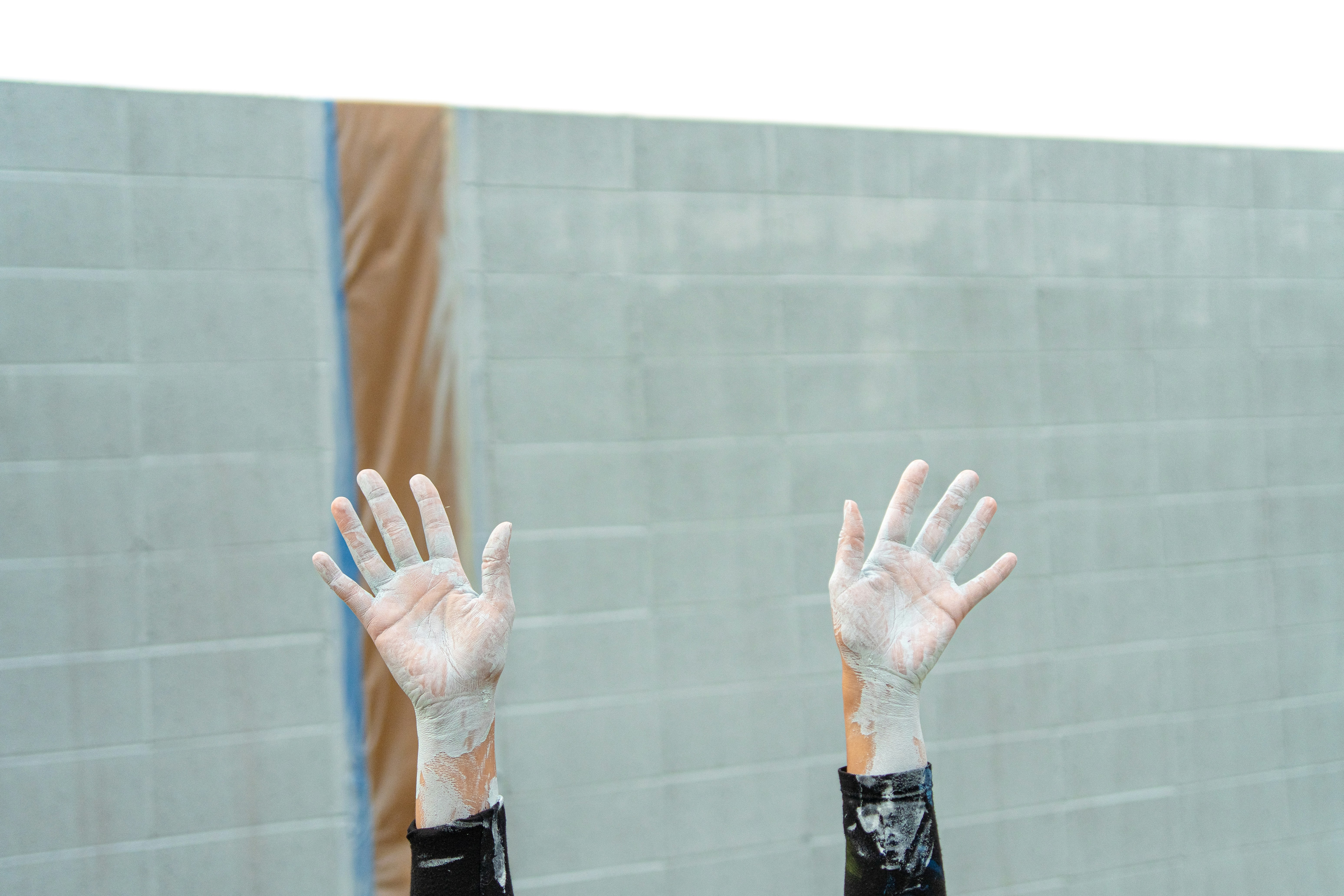 Hands are raised against a concrete brick wall.