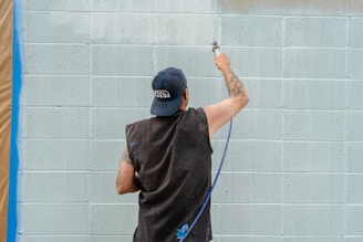 A man sprays paint on a cinder block wall.