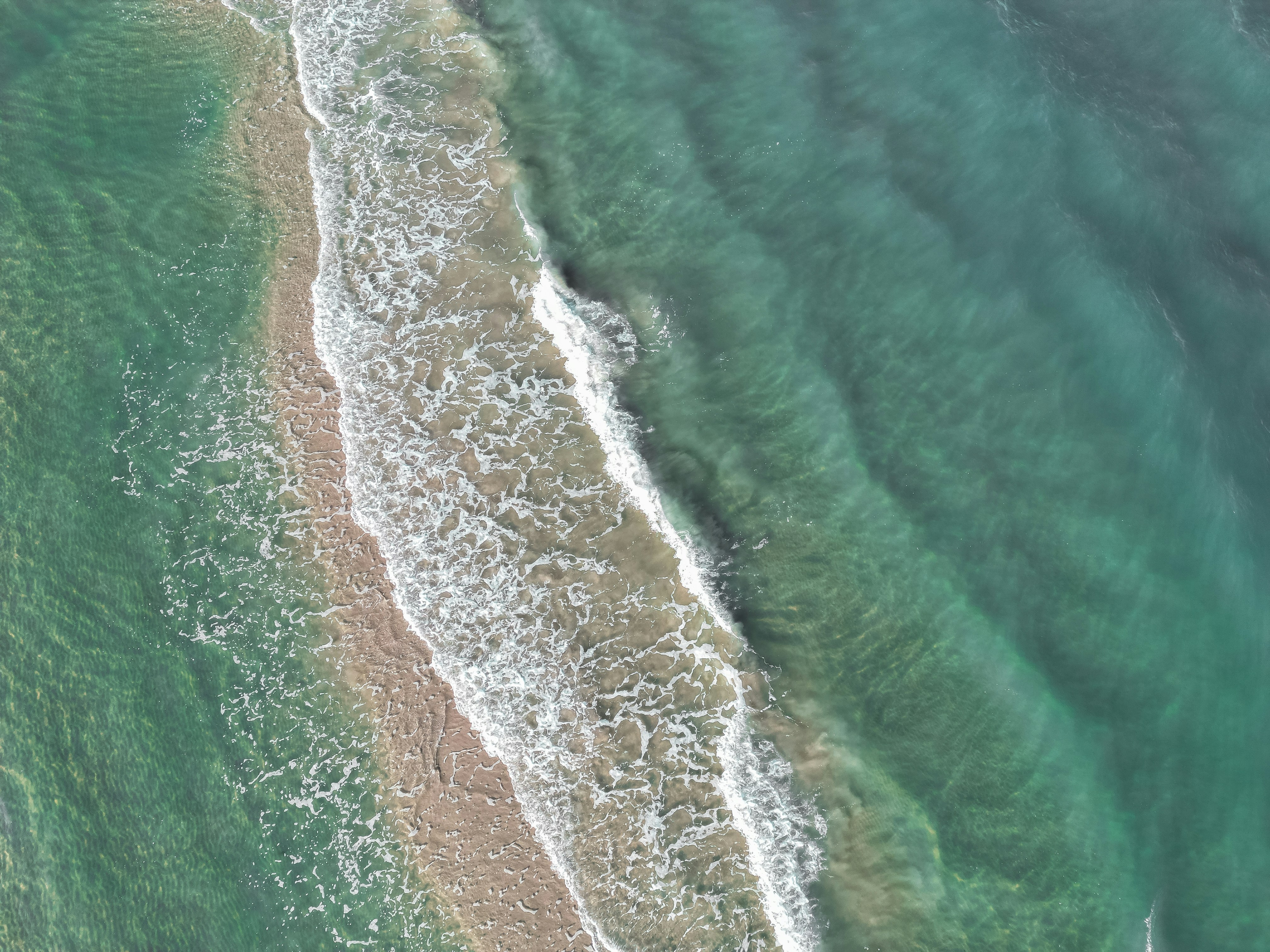 Waves crash on a sandy beach in the turquoise sea.