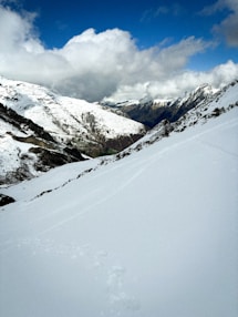 Snow-covered mountains beneath a cloudy blue sky.
