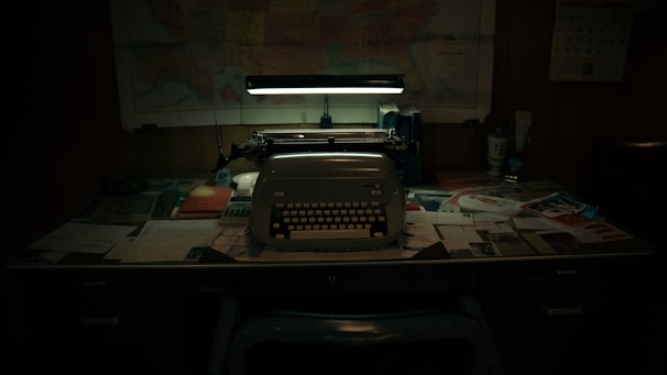 Typewriter sits on a cluttered desk in dim lighting.