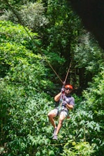 Man ziplining through a lush, green forest.