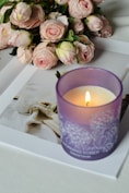 A lit candle and roses sit on a book.