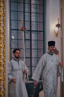 Two orthodox priests holding candles walk.
