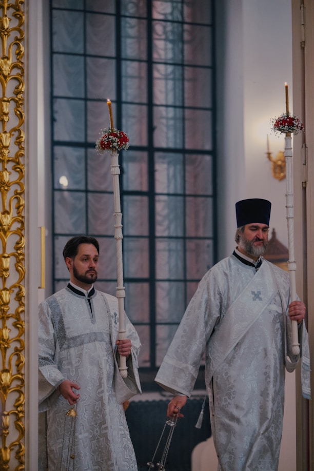 Two orthodox priests holding candles walk.