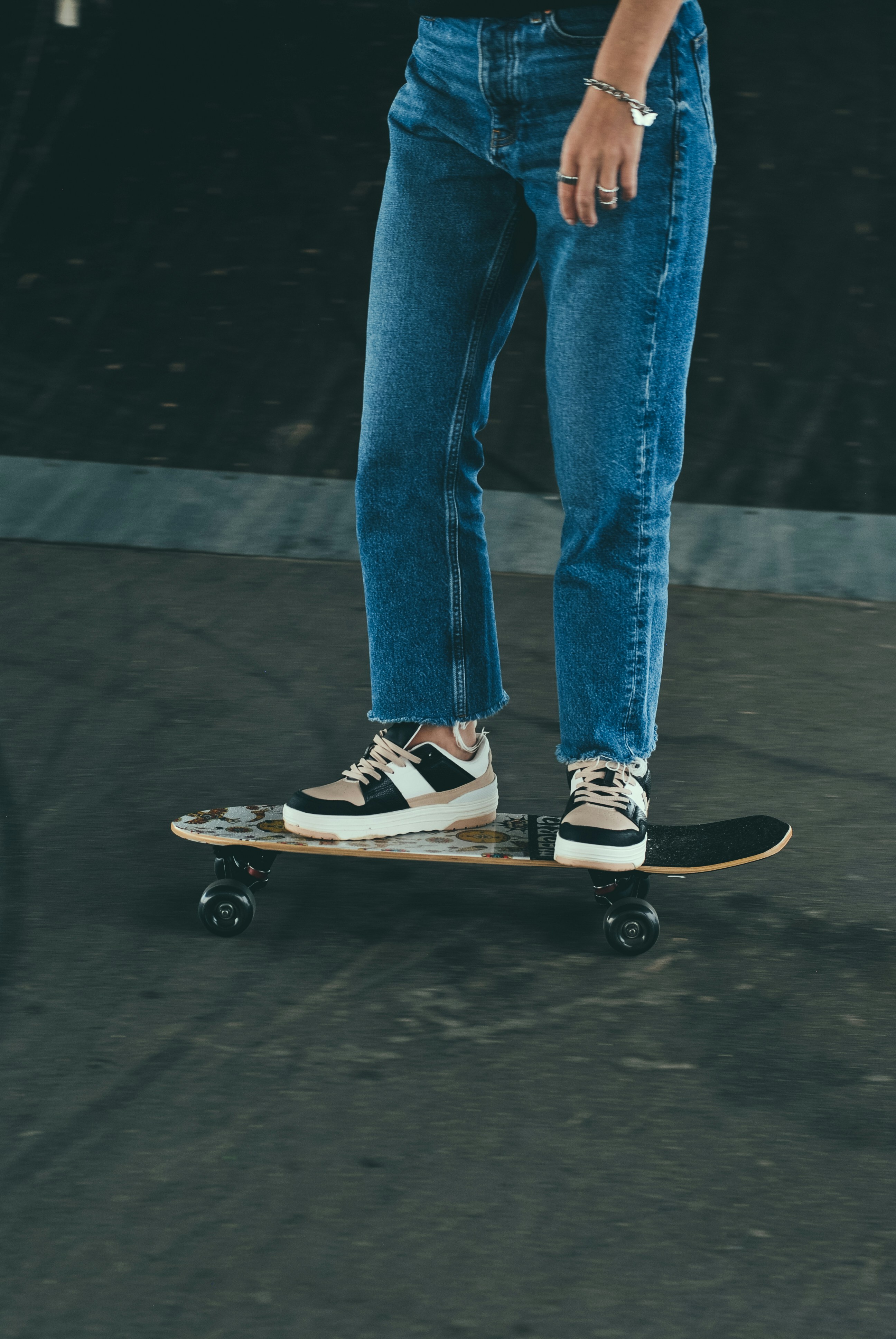 Person stands on a skateboard, wearing jeans and sneakers.