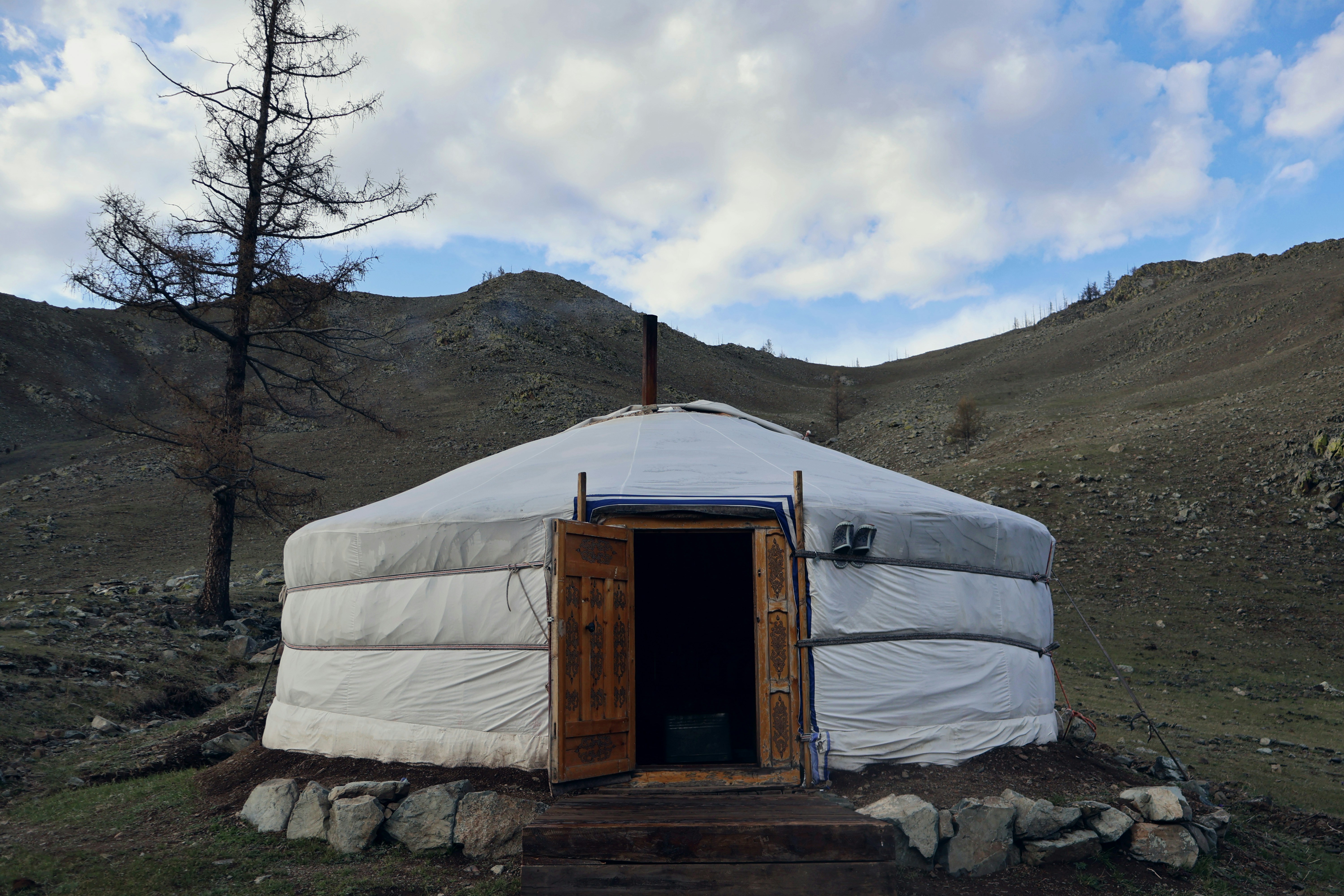 A mongolian yurt sits in a scenic, hilly landscape.