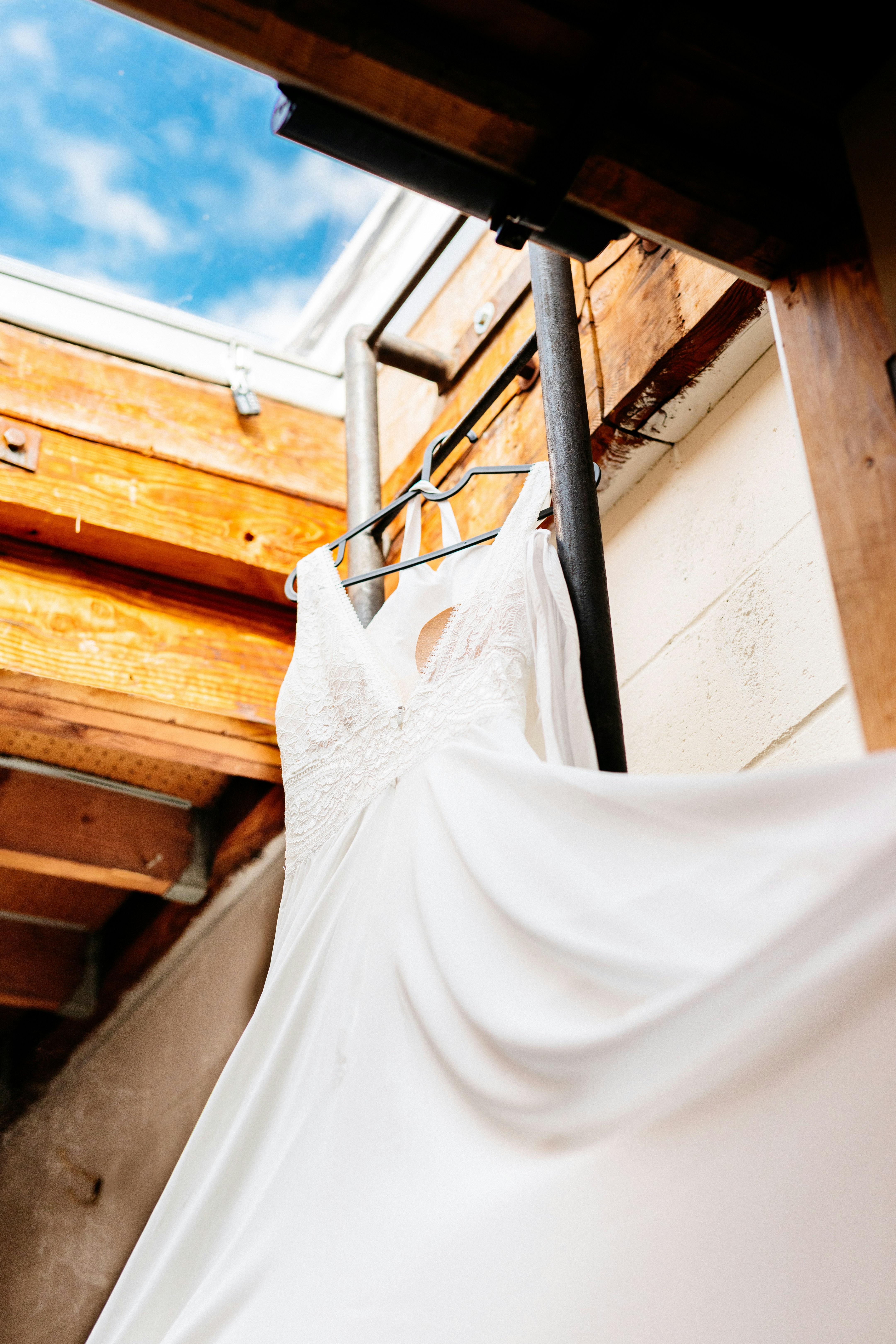 Wedding dress hangs from a ladder, under the sky.