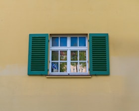 Window with green shutters against a yellow wall.